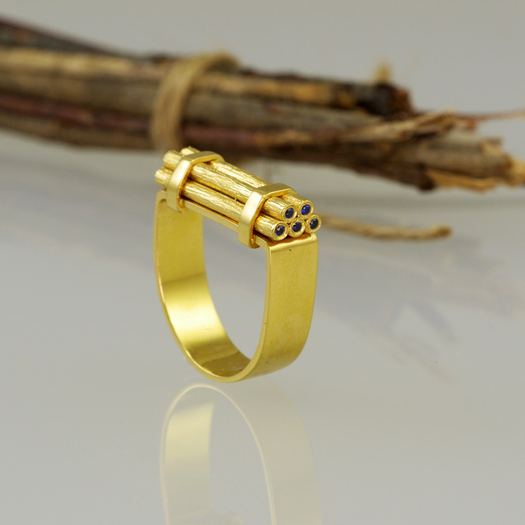 A unique, handmade gold ring that draws its inspiration from stacks of wood piled together. Tiny sparkling Sapphires were added to get that extra color and glow. Stacked wood lies in the background