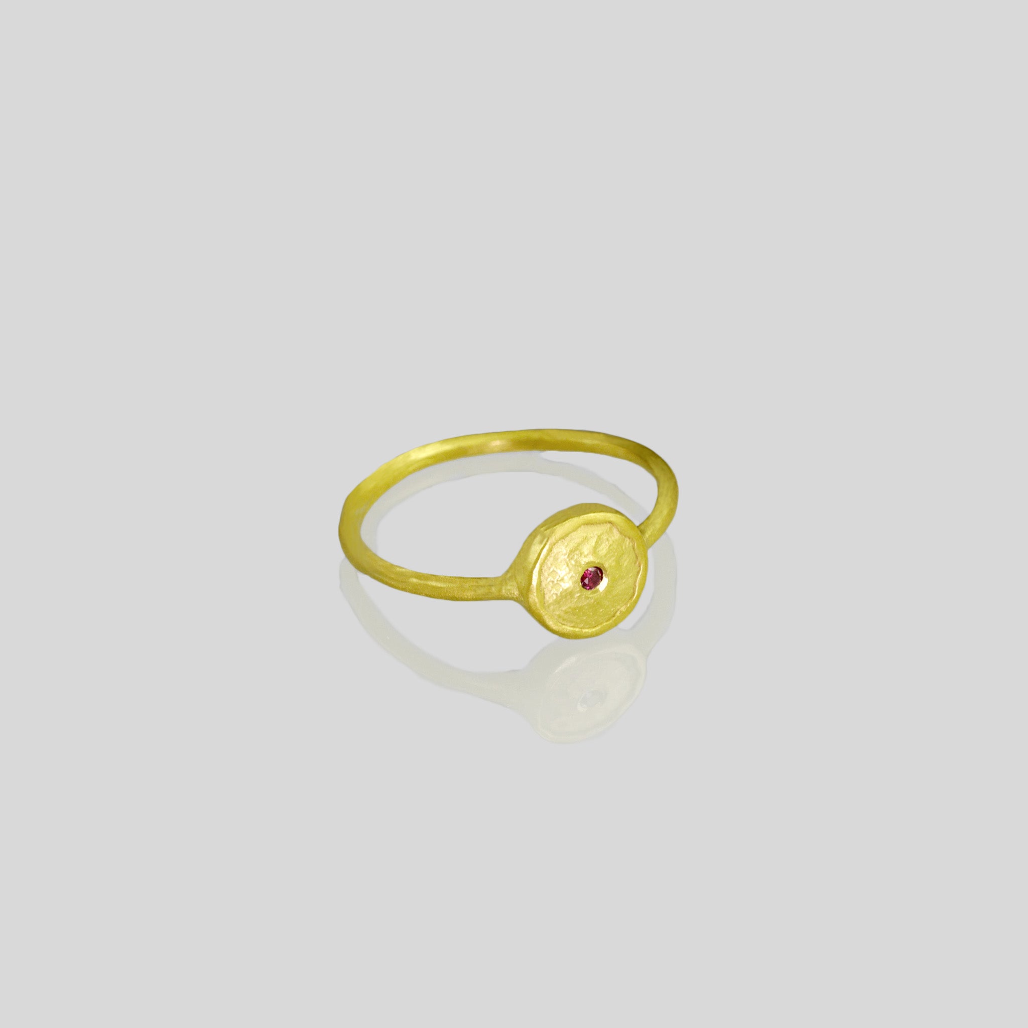 Hand-crafted 18k Gold Ring with a small Ruby set in the center of a circular plate, resembling a shining star in the sky. Delicate and elegant, radiating brilliance.