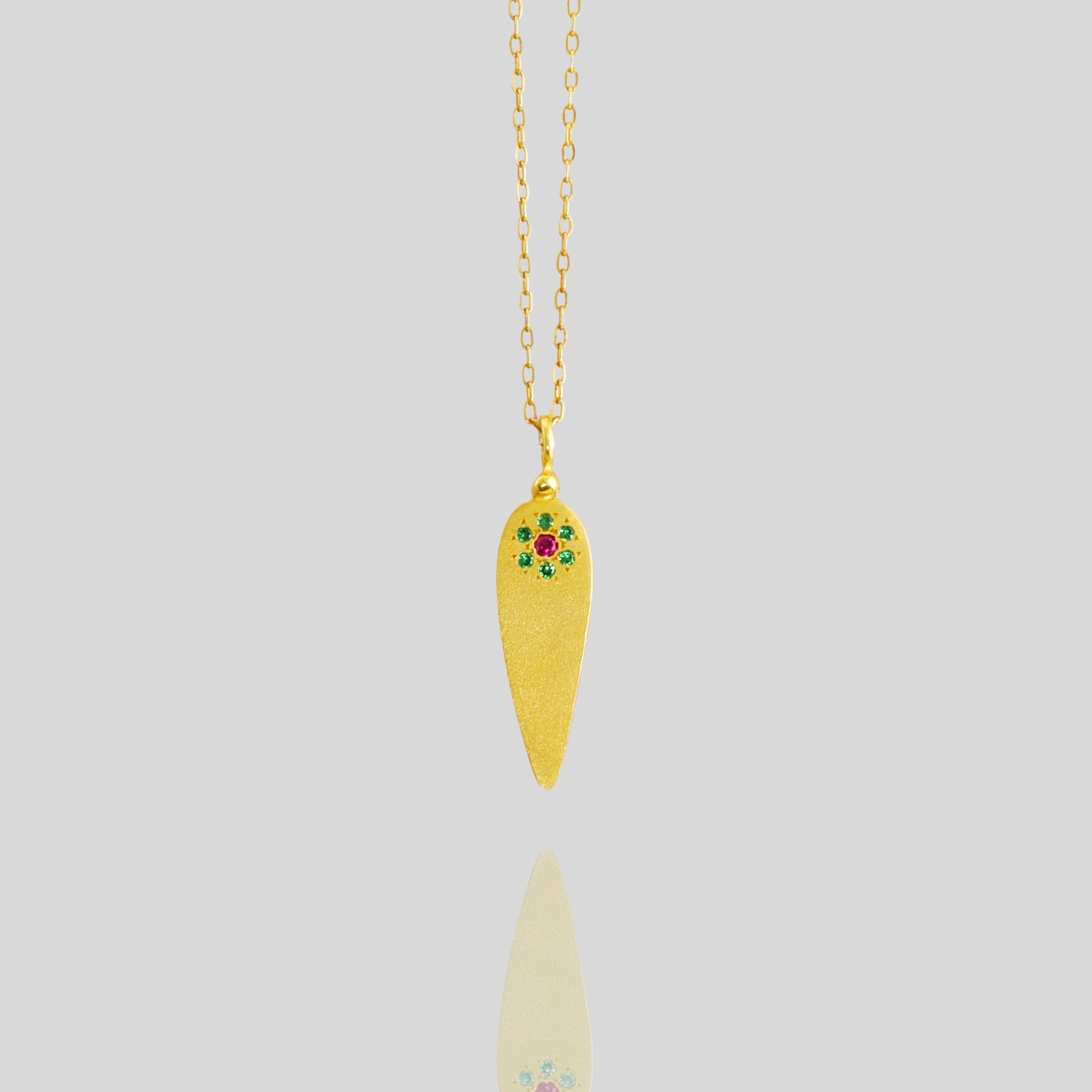 close up of 18k Yellow Gold pendant crafted in the form of a delicate leaf, adorned with ruby and emerald gemstones arranged to resemble a small, intricate flower.