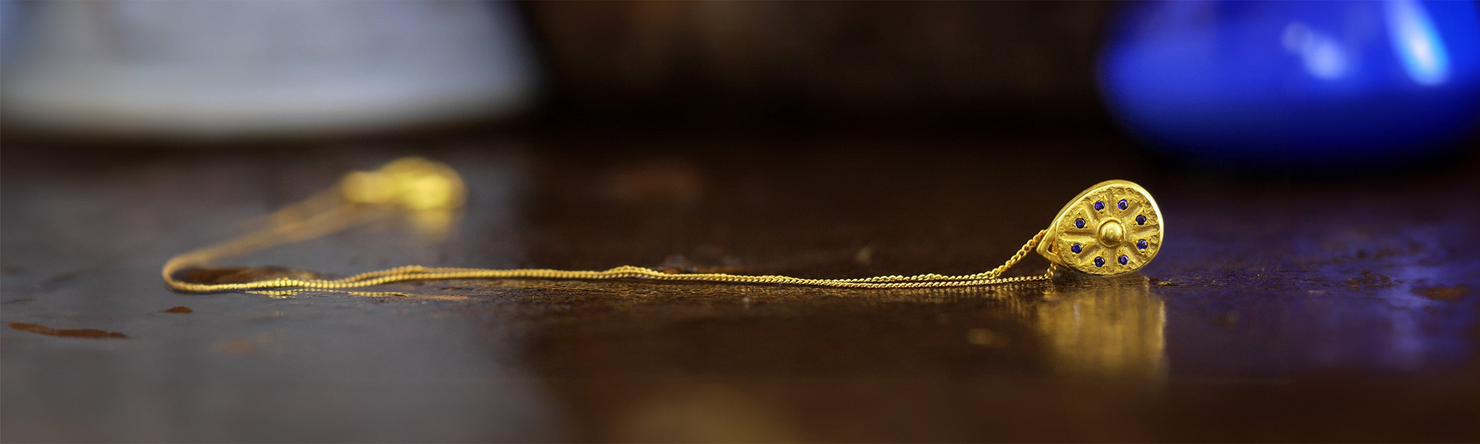 An exquisite gold pendant crafted to resemble an ancient sundial clock, featuring delicate sapphires carefully placed at the edges between each clock hand marker, radiating luxury and timeless elegance for the necklaces collection banner.