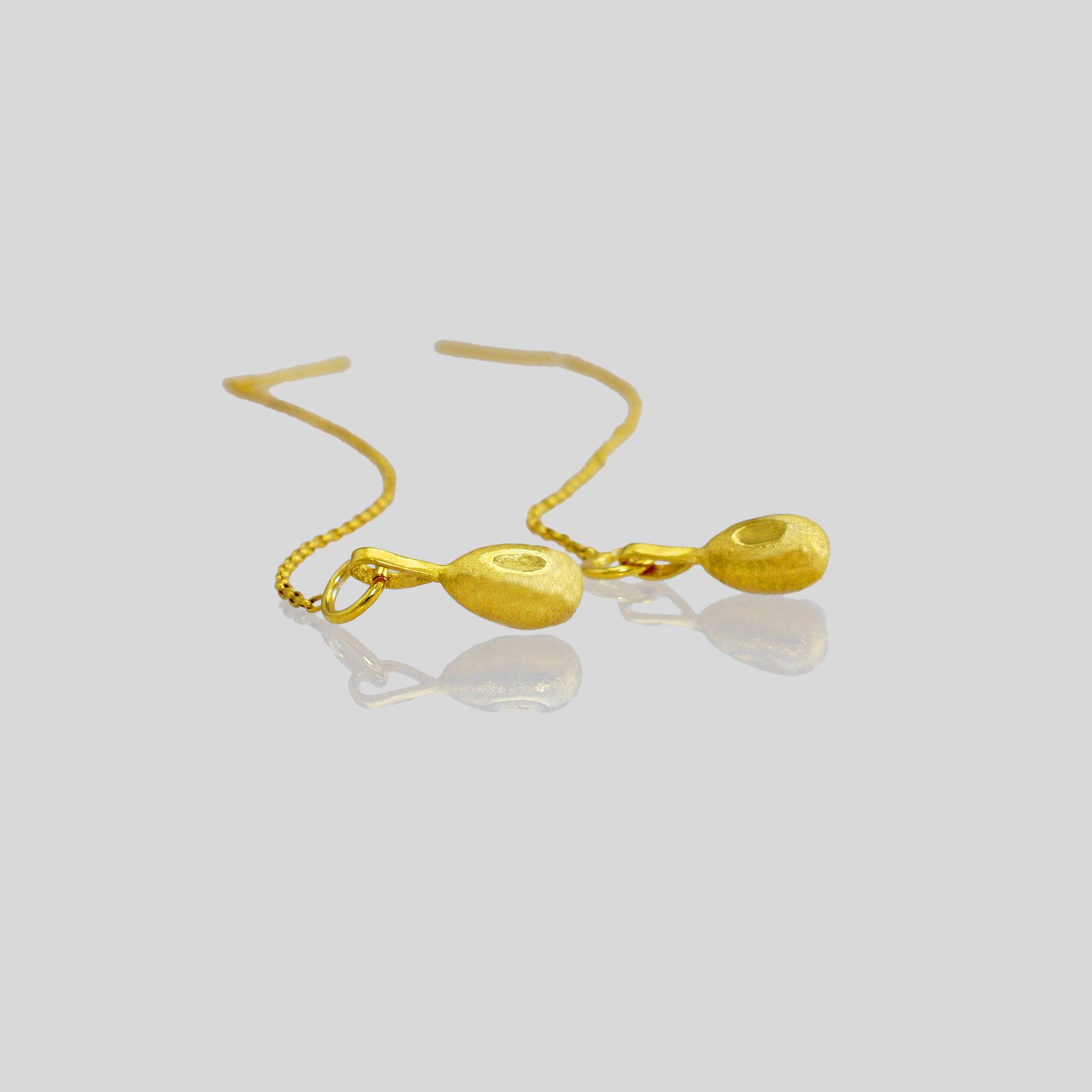 Close up of nature-inspired gold earrings with delicate chains and needle-tip attachments, embodying graceful and organic movement.