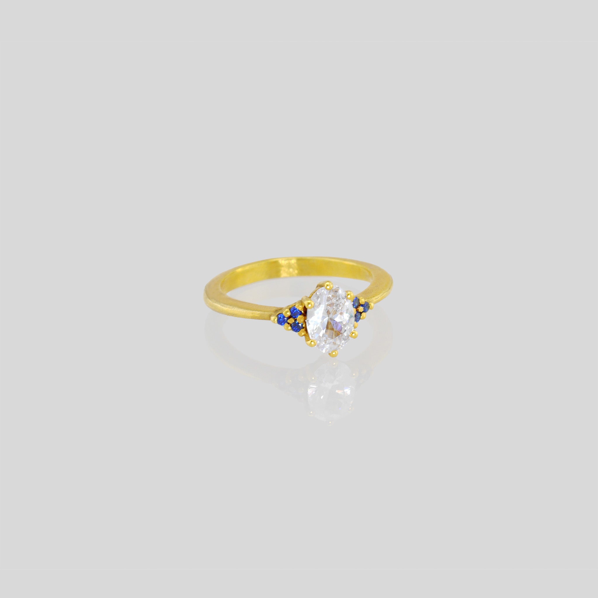 Gold engagement ring with oval central diamond and three tiny Sapphires on each side. Timeless elegance with a touch of color, perfect for an elegant proposal.