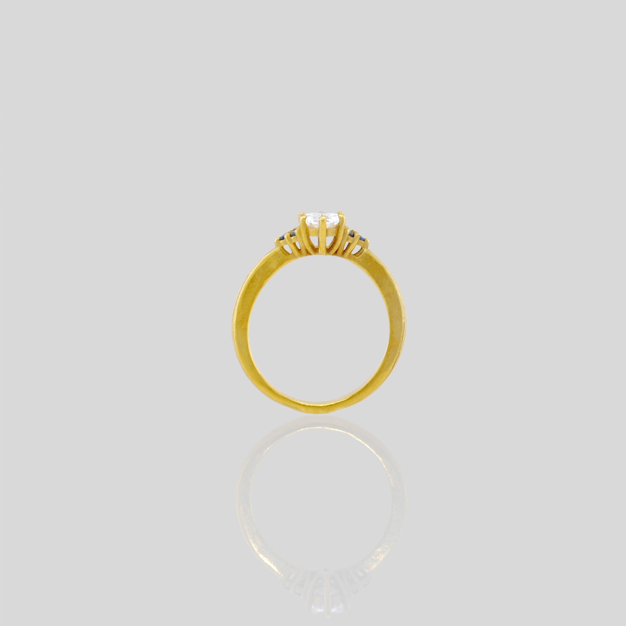 Side angle of our Gold engagement ring with oval central diamond and three tiny Sapphires on each side. Timeless elegance with a touch of color, perfect for an elegant proposal.