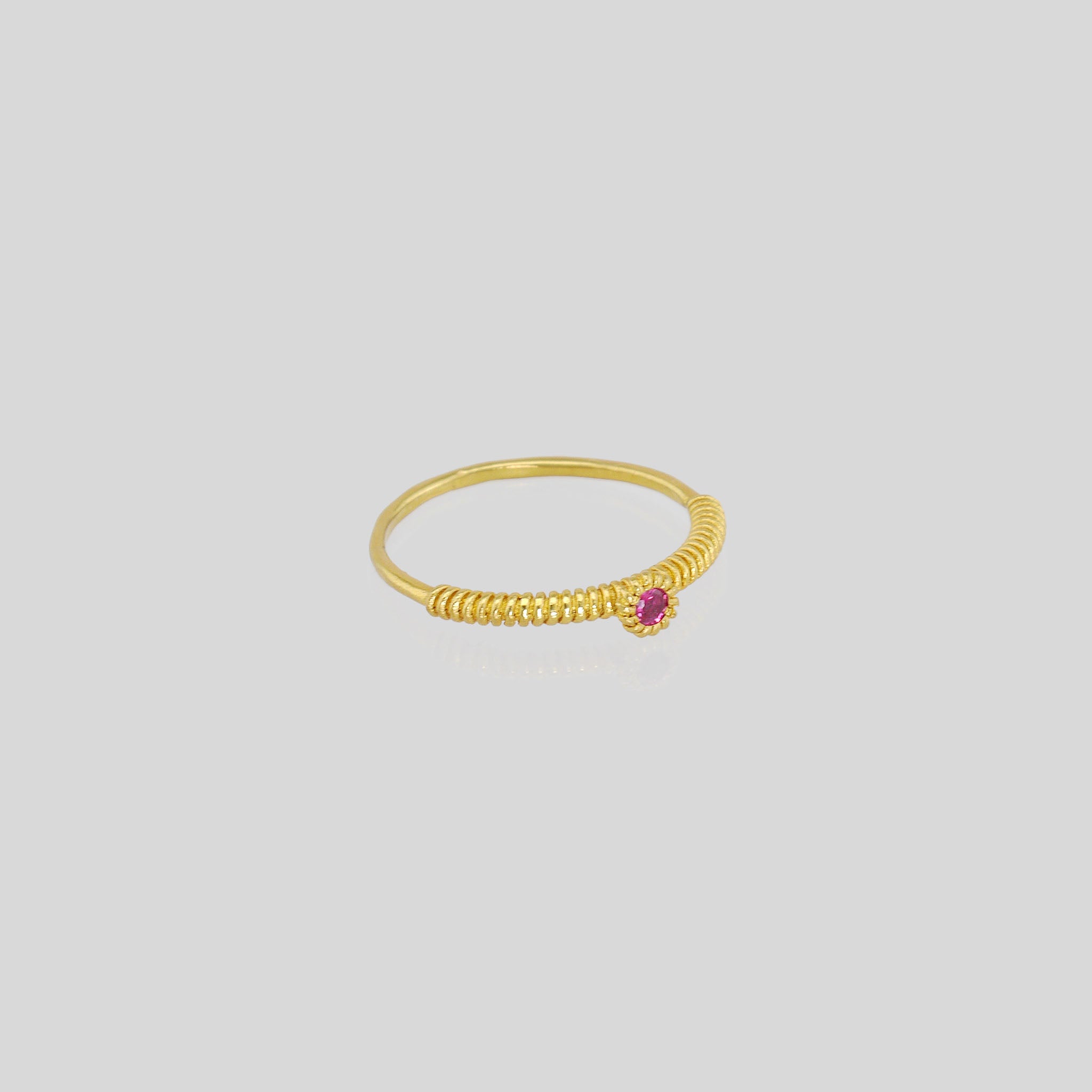 A thin gold ring with a coiled gold string, showcasing a vivid Ruby at its center. Elegant and charming, it radiates subtle allure.