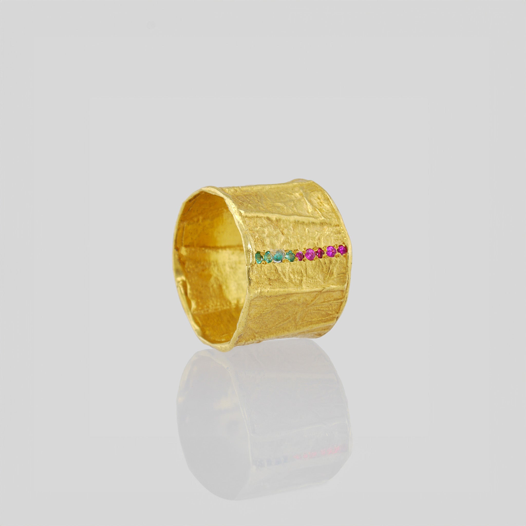 Handcrafted gold ring featuring a wide band with a distinct textured surface achieved through Kami's paper modeling technique. Embellished with miniature rubies and emeralds, this ring exudes a one-of-a-kind, magnificent charm.