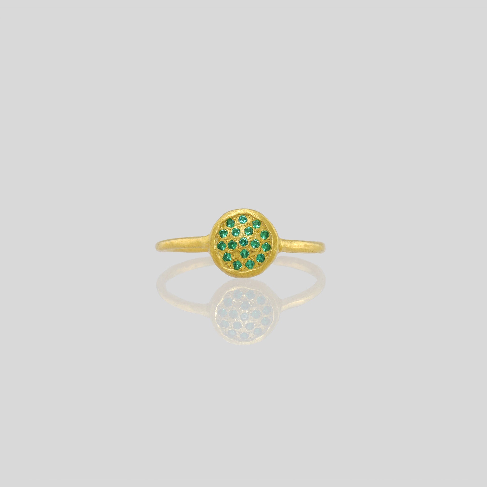 Front view of a Delicate hand-made gold ring with a circular plate set with tiny Emerald gemstones. The sparkle from the stones resembles a starry night.