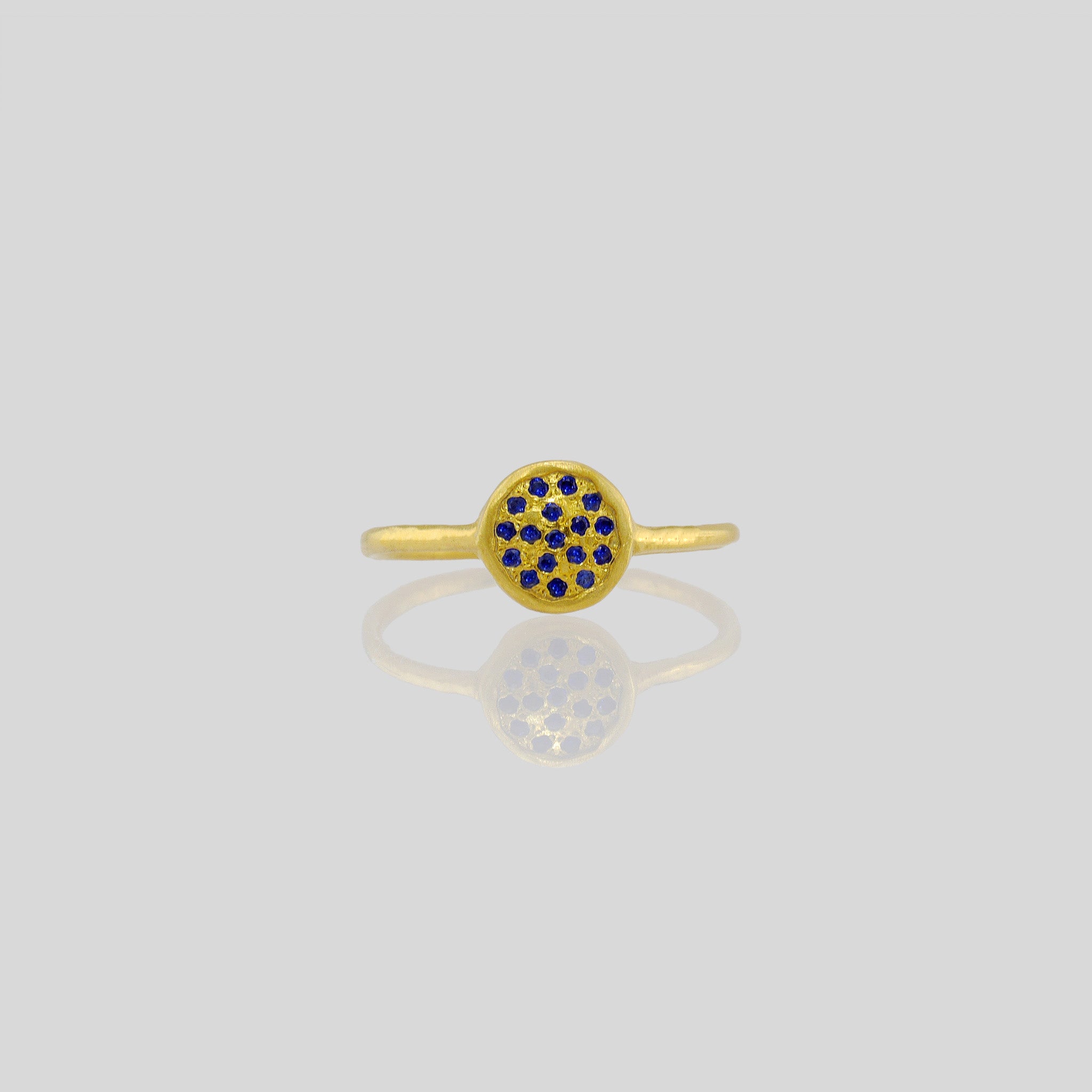Front view of a Delicate hand-made gold ring with a circular plate set with tiny Sapphires. The sparkle from the stones resembles a starry night.