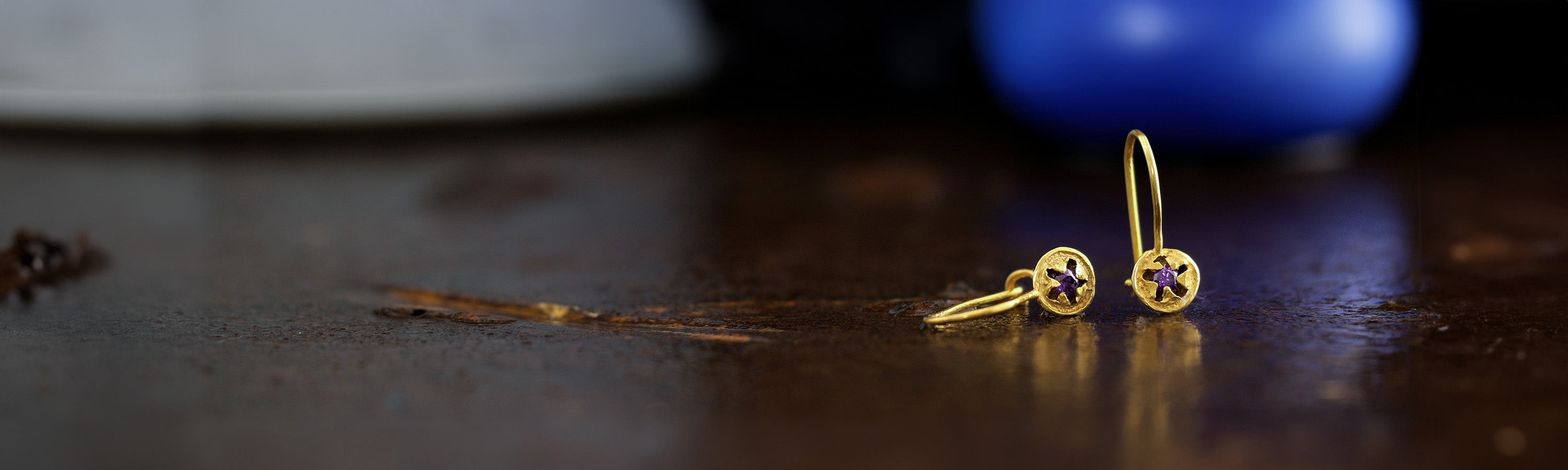 Banner image for Kami-Jewelry's Earrings collection displaying delicate drop earrings from the collection, crafted from yellow gold in the shape of eucalyptus seeds, each with a central amethyst stone inlaid, symbolizing a seed about to hatch, against an elegant backdrop.