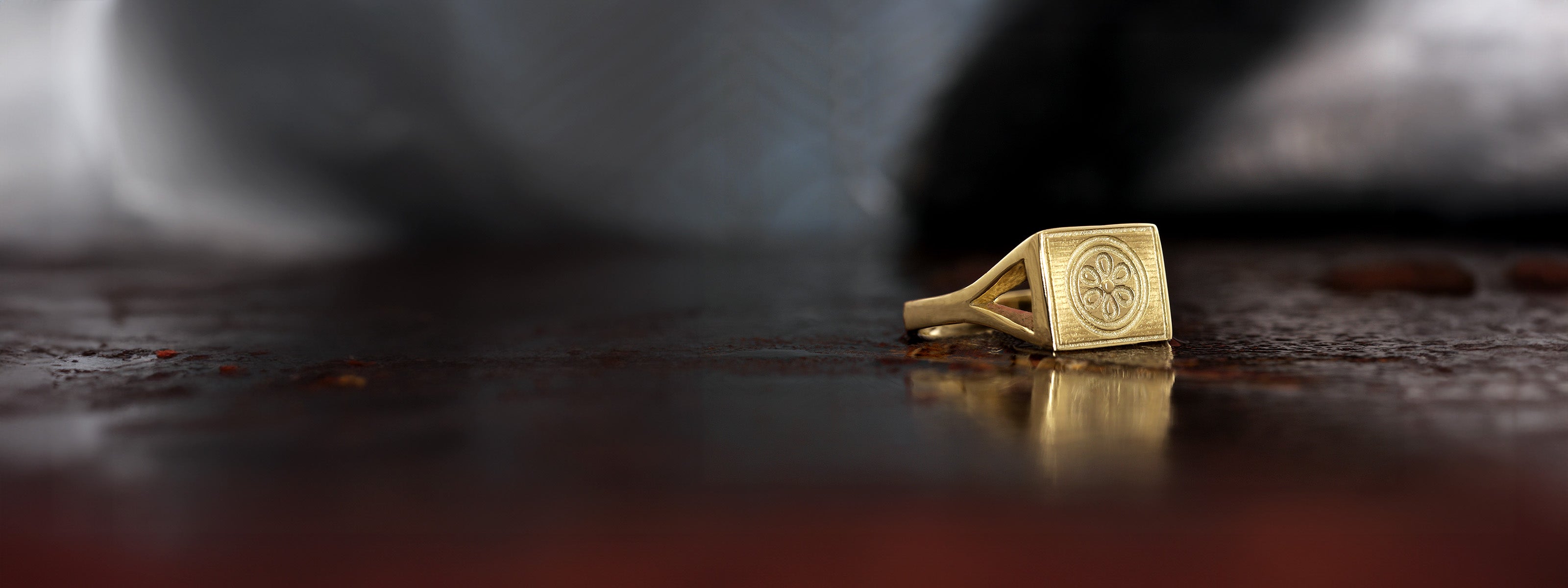 A timeless 18k gold seal ring resting on a rugged, textured iron surface with a dreamy background.