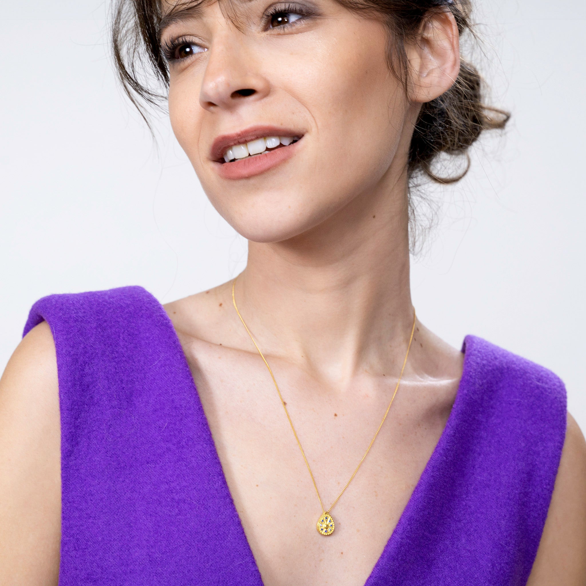 Model showcasing a unique gold sundial clock-shaped pendant, its edges embellished with tiny sapphires, offering a luxurious and historical dimension to any ensemble.