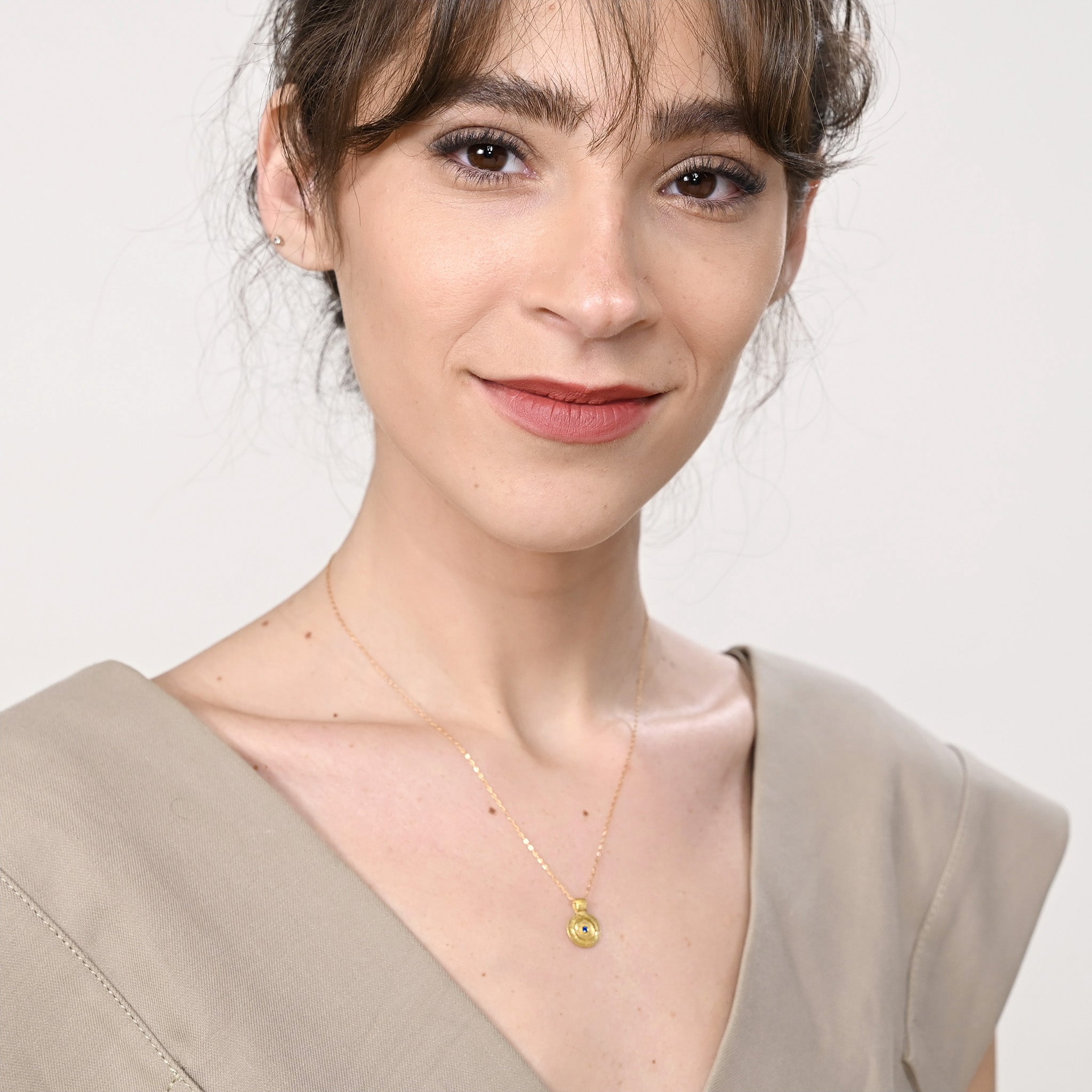 model displaying Pharaohs I - Ancient round gold pendant with a vivid Sapphire gemstone at its center, reminiscent of the opulent jewelry of the Egyptian Pharaohs' era, crafted from yellow gold.