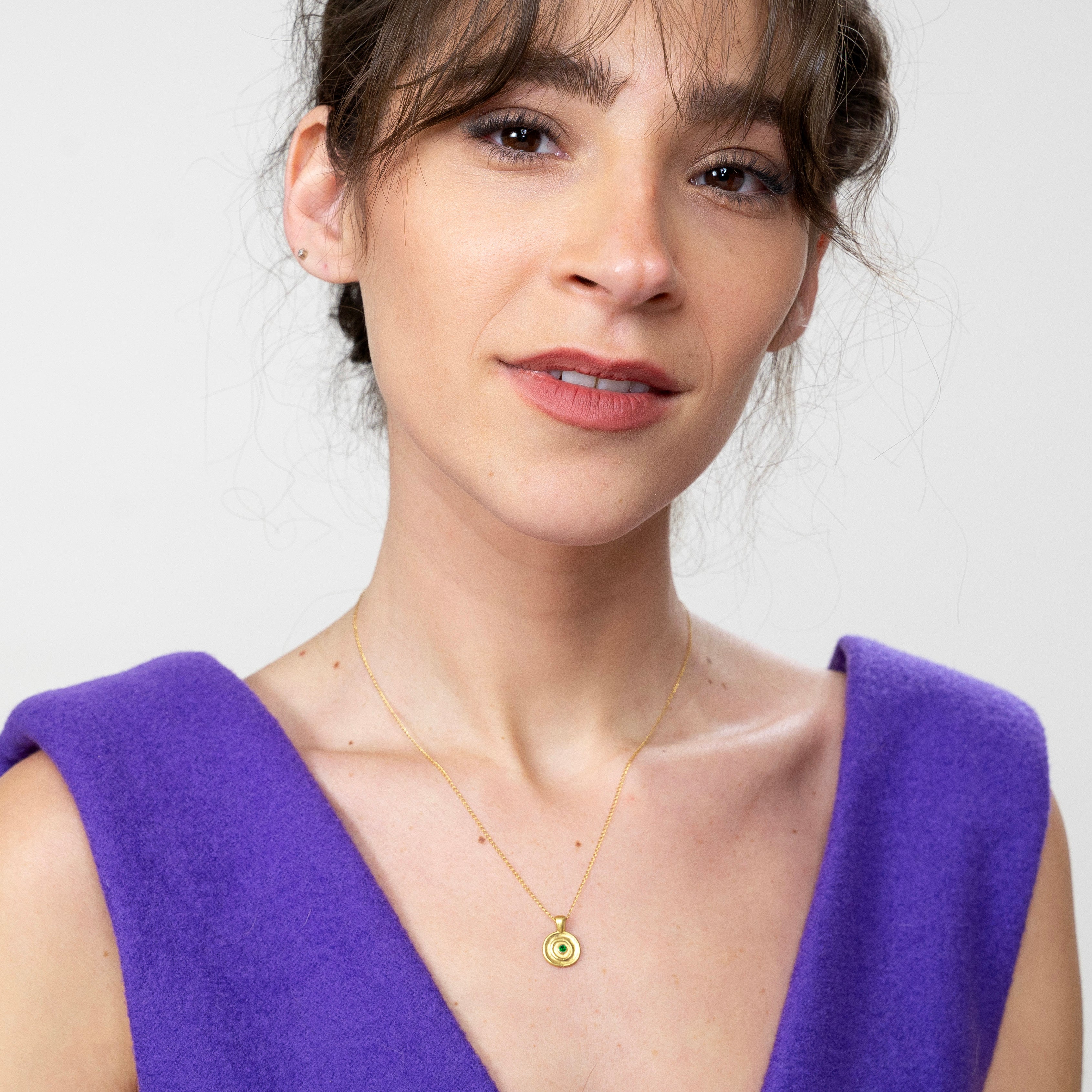 Model gracefully wearing the Pharaohs II round gold pendant, featuring a lustrous Emerald at its center, echoing the sophisticated craftsmanship of ancient Egyptian Pharaohs' jewelry.