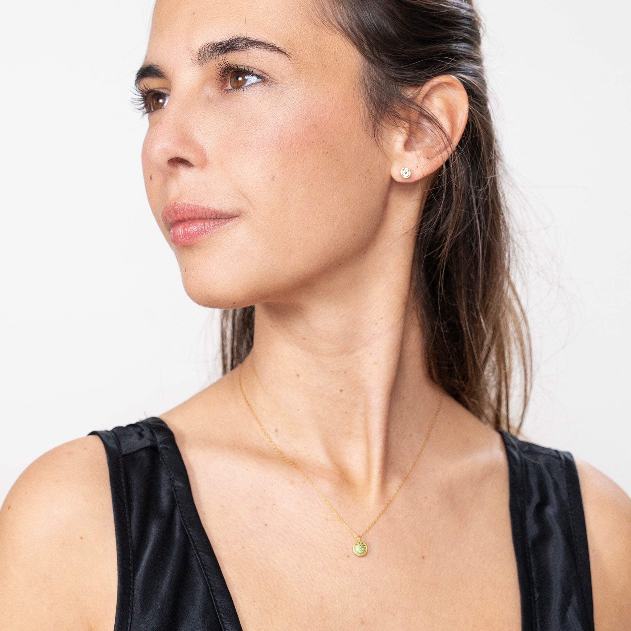 Model elegantly showcases the Starlit gold pendant, its gold plate adorned with Emeralds that glisten like stars against the night sky, highlighting its exquisite craftsmanship.