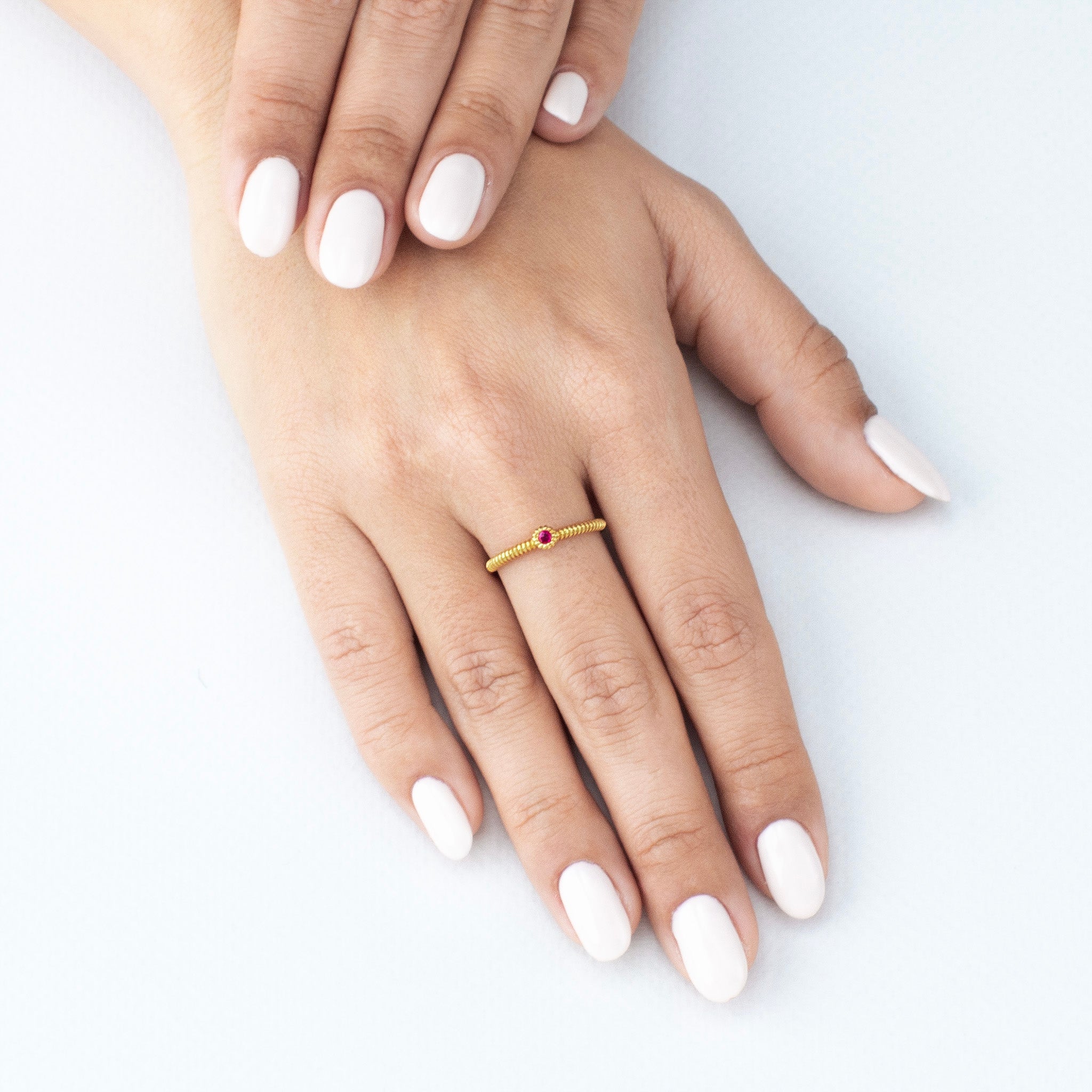Model displaying a delicate gold coiled ring, featuring a ruby gemstone, enhancing the finger with its poetic elegance.