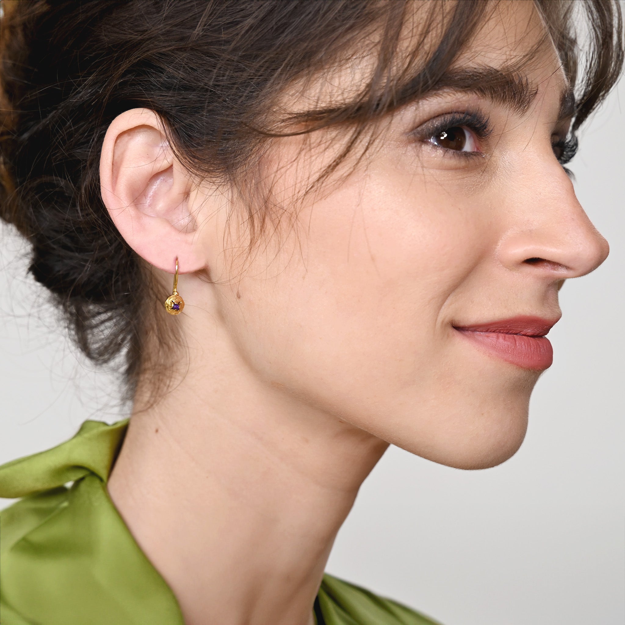 Model wearing delicate yellow gold drop earrings shaped like eucalyptus seeds, with a central amethyst stone, showcasing elegance and natural inspiration.