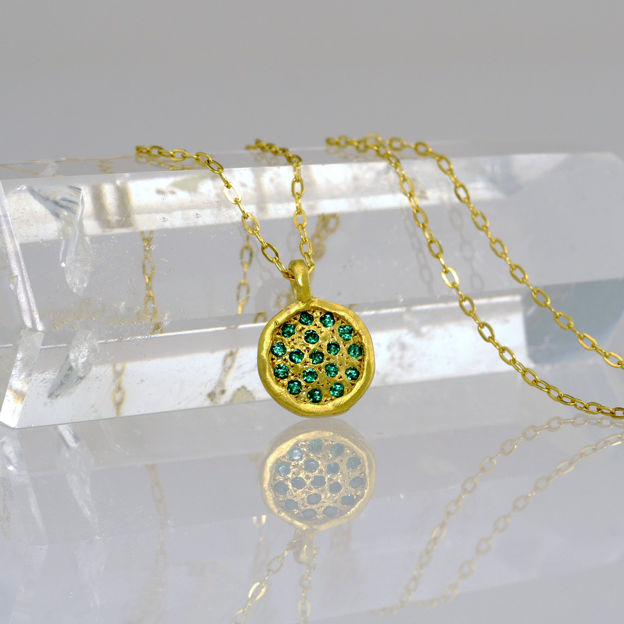 Close up of Starlit gold pendant, meticulously crafted from Yellow Gold with a small gold plate embellished with scattered Emeralds, mirroring the enchanting allure of a starry night.