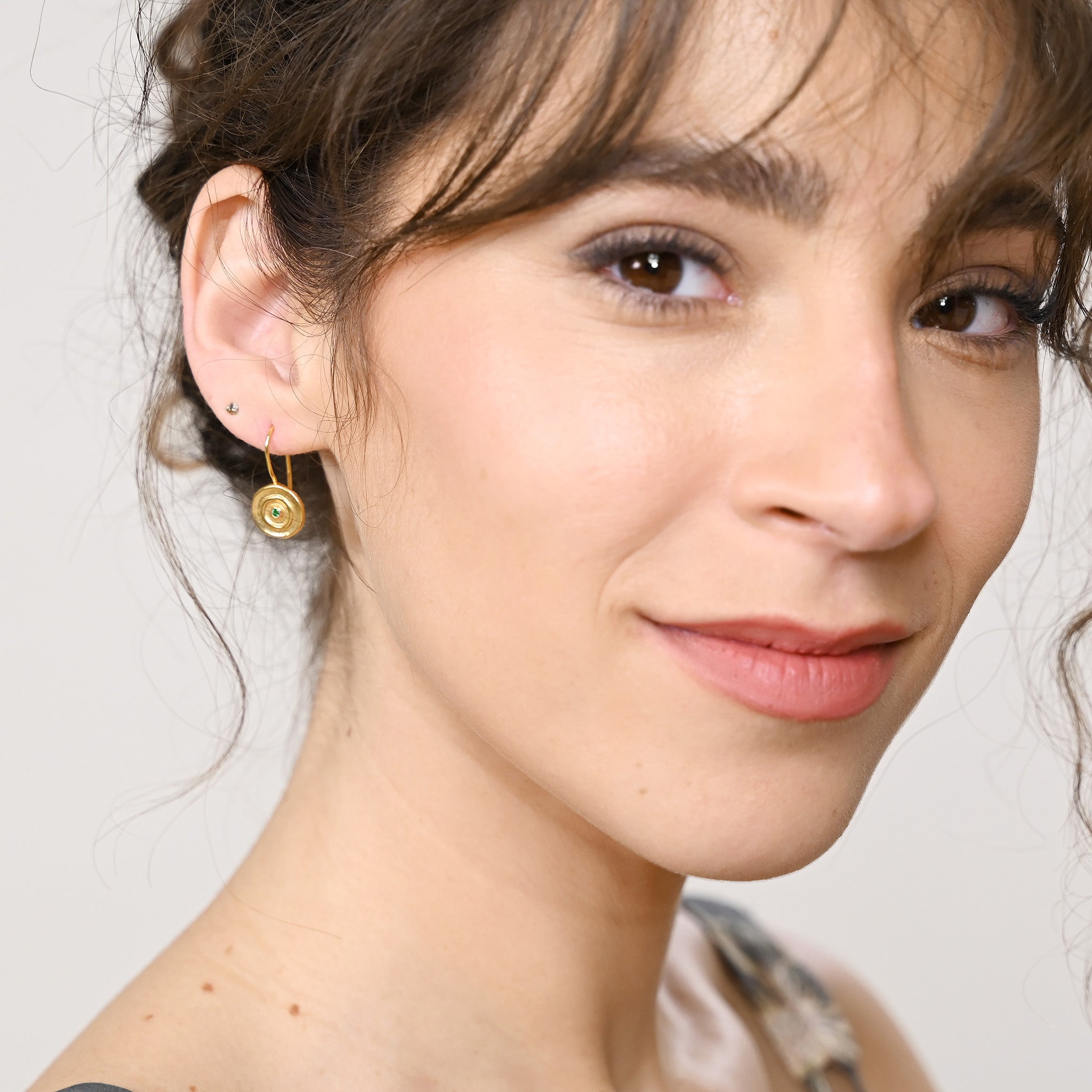 Model displaying an Hand-made 18k gold round drop earrings with a central Emerald gemstone, inspired by ancient Egyptian Pharaohs' gold jewelry.