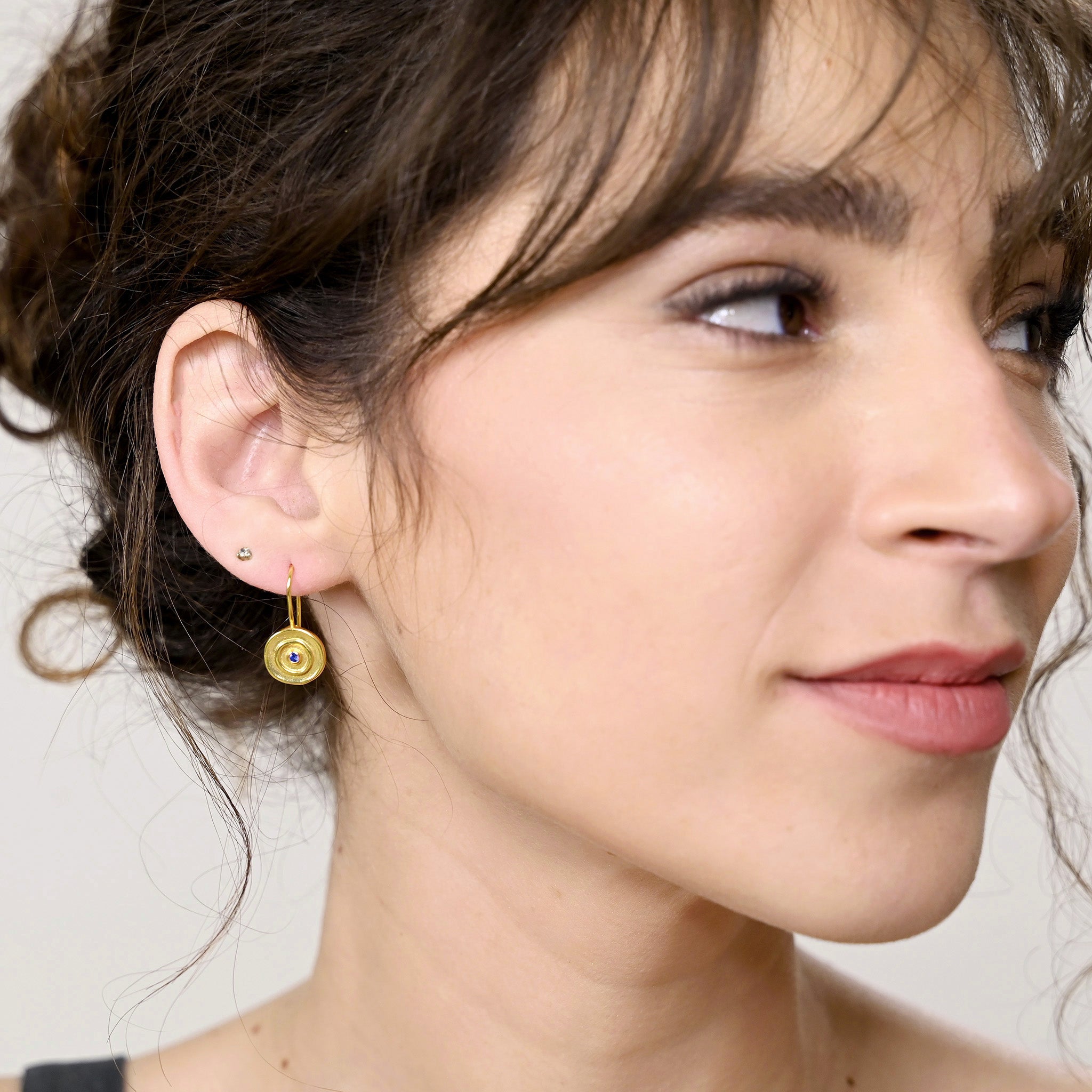 Model displaying an Hand-made 18k gold round drop earrings with a central Sapphire gemstone, inspired by ancient Egyptian Pharaohs' gold jewelry.