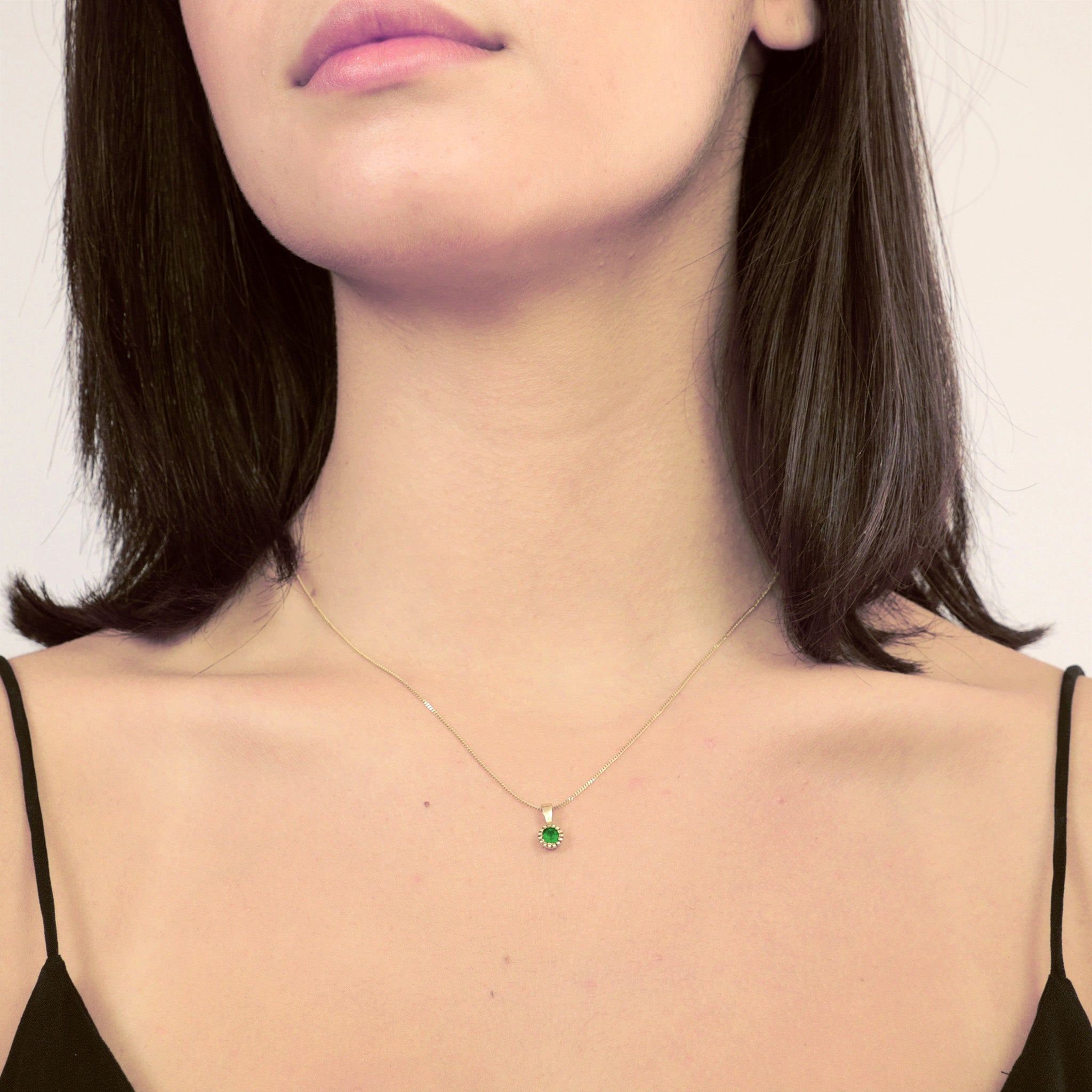 Model wearring an Elegant round gold pendant with embroidered texture and central Emerald, exuding classic sophistication.