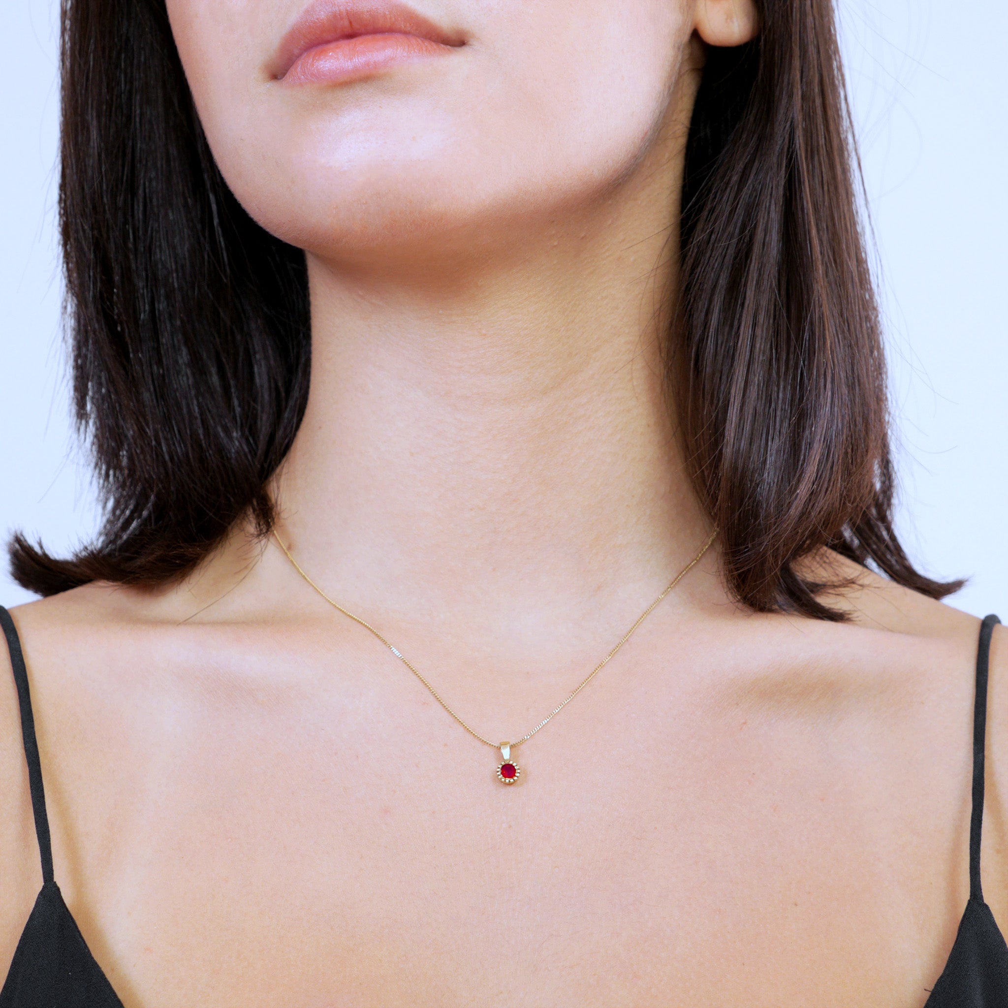 Model wearring an Elegant round gold pendant with embroidered texture and central Ruby, exuding classic sophistication.