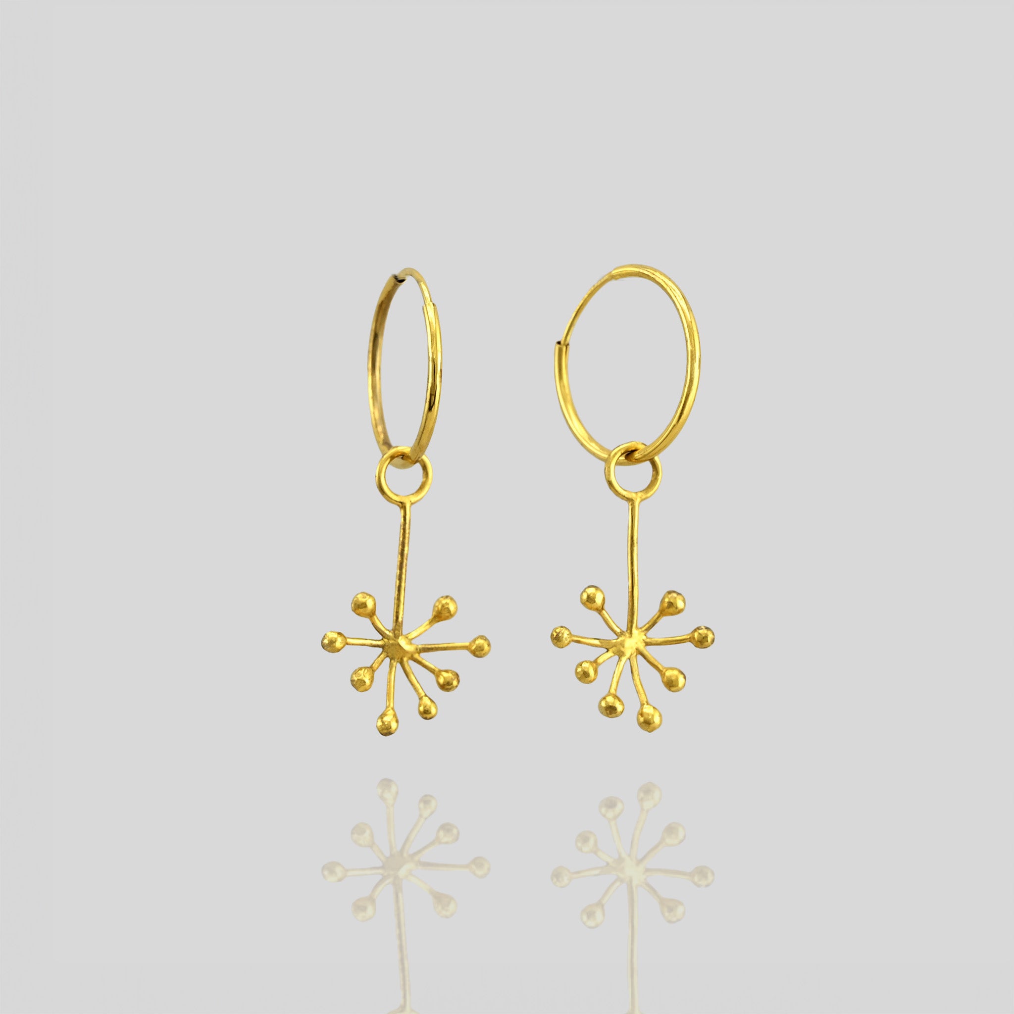 Close up of delicate 18k yellow gold earrings featuring an intricate snowflake design formed by thin, radiating gold lines. The design exudes a subtle yet playful aesthetic.