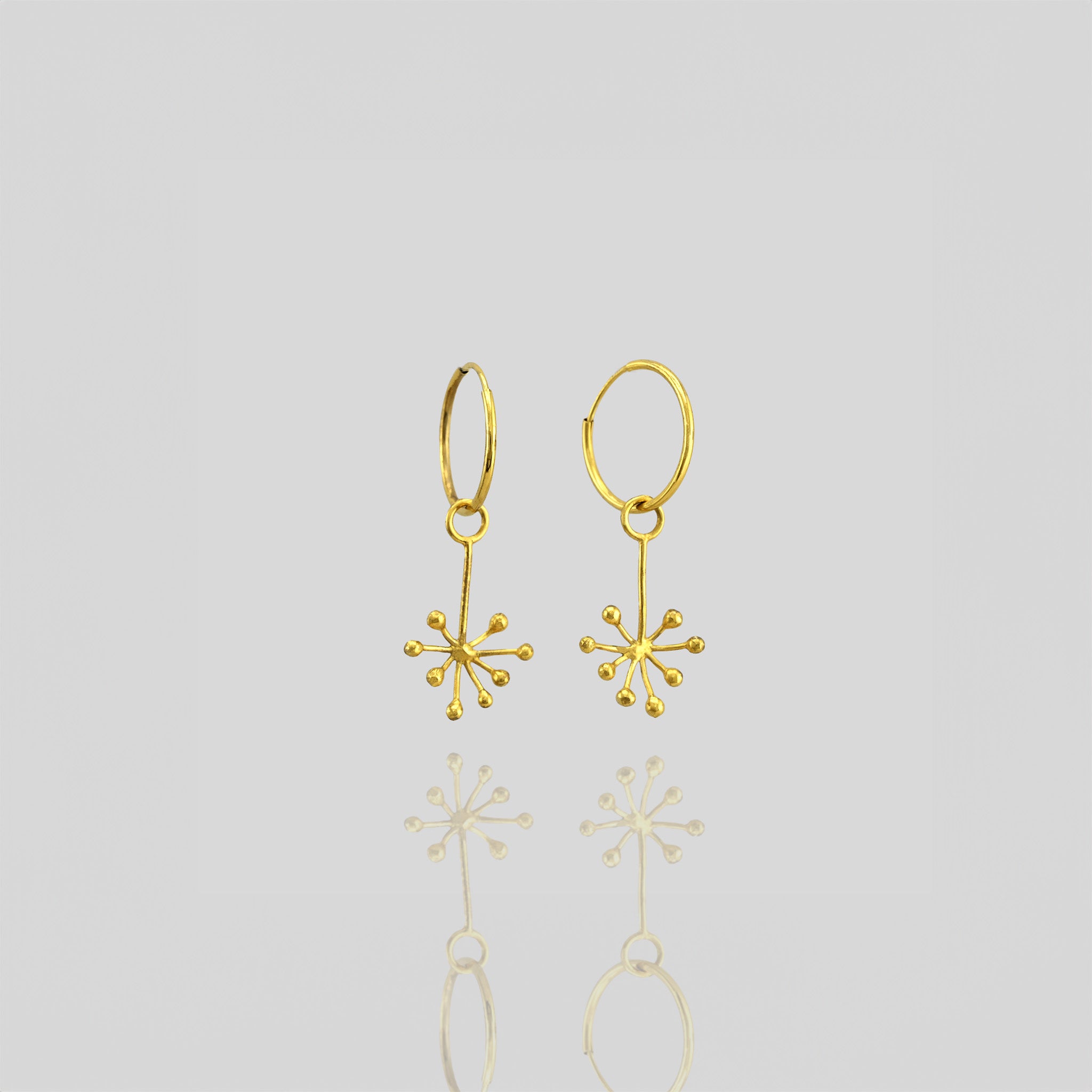 Delicate 18k yellow gold earrings featuring an intricate snowflake design formed by thin, radiating gold lines. The design exudes a subtle yet playful aesthetic.