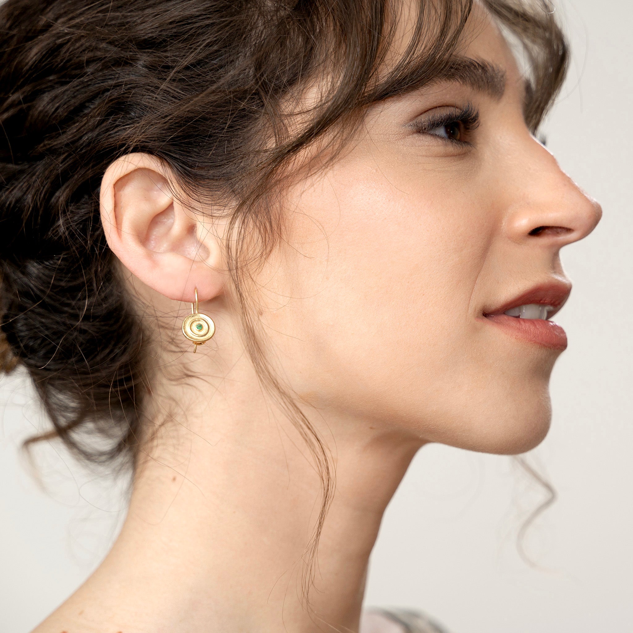 Model displaying an Hand-made 18k gold round drop earrings with a central Emerald gemstone, inspired by ancient Egyptian Pharaohs' gold jewelry.