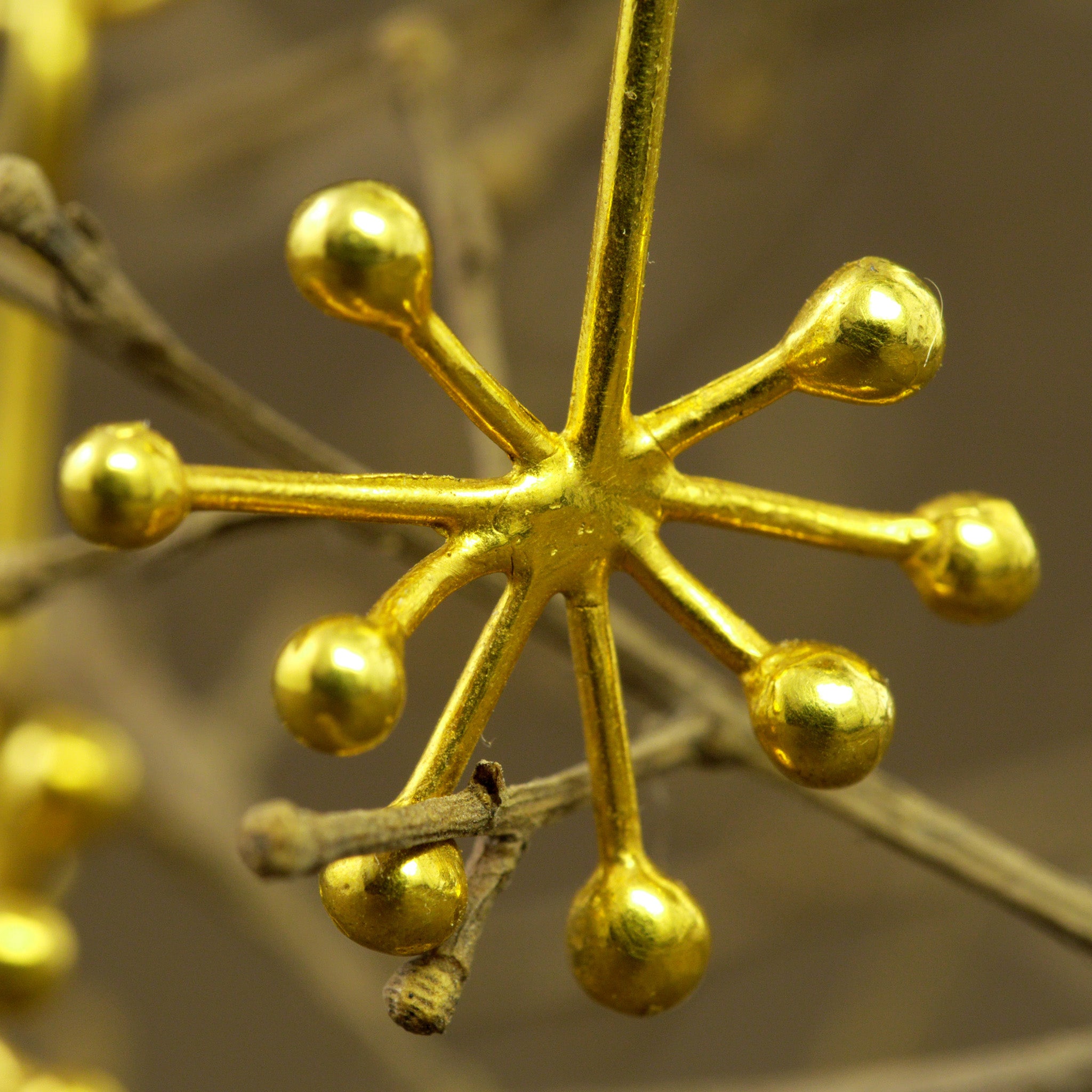 close up of delicate 18k yellow gold earrings featuring an intricate snowflake design formed by thin, radiating gold lines. The design exudes a subtle yet playful aesthetic.