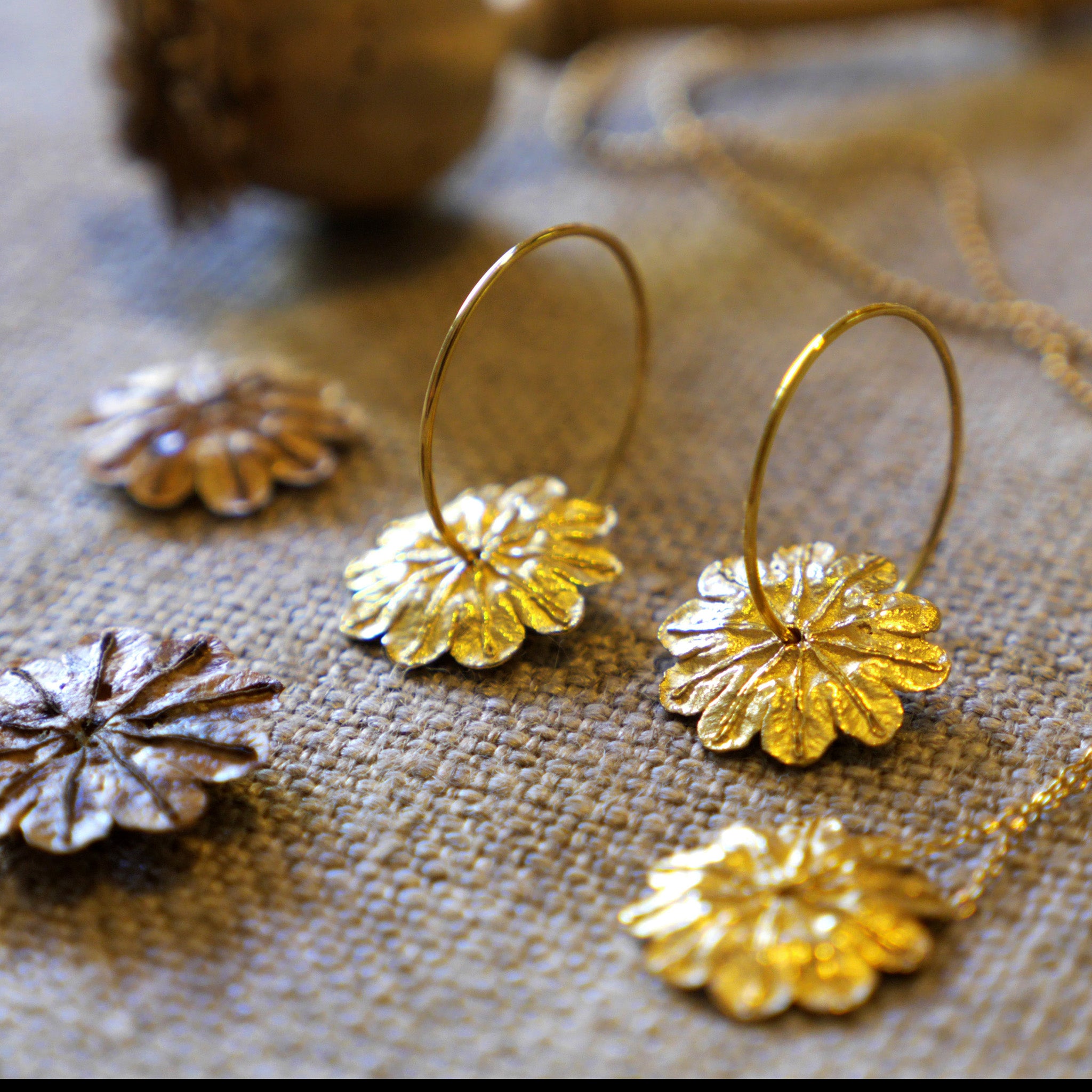 18k Gold Poppy Flower Hoop Earrings showcasing captivating beauty rest atop a natural surface embellished with real dried poppy seeds scattered around.