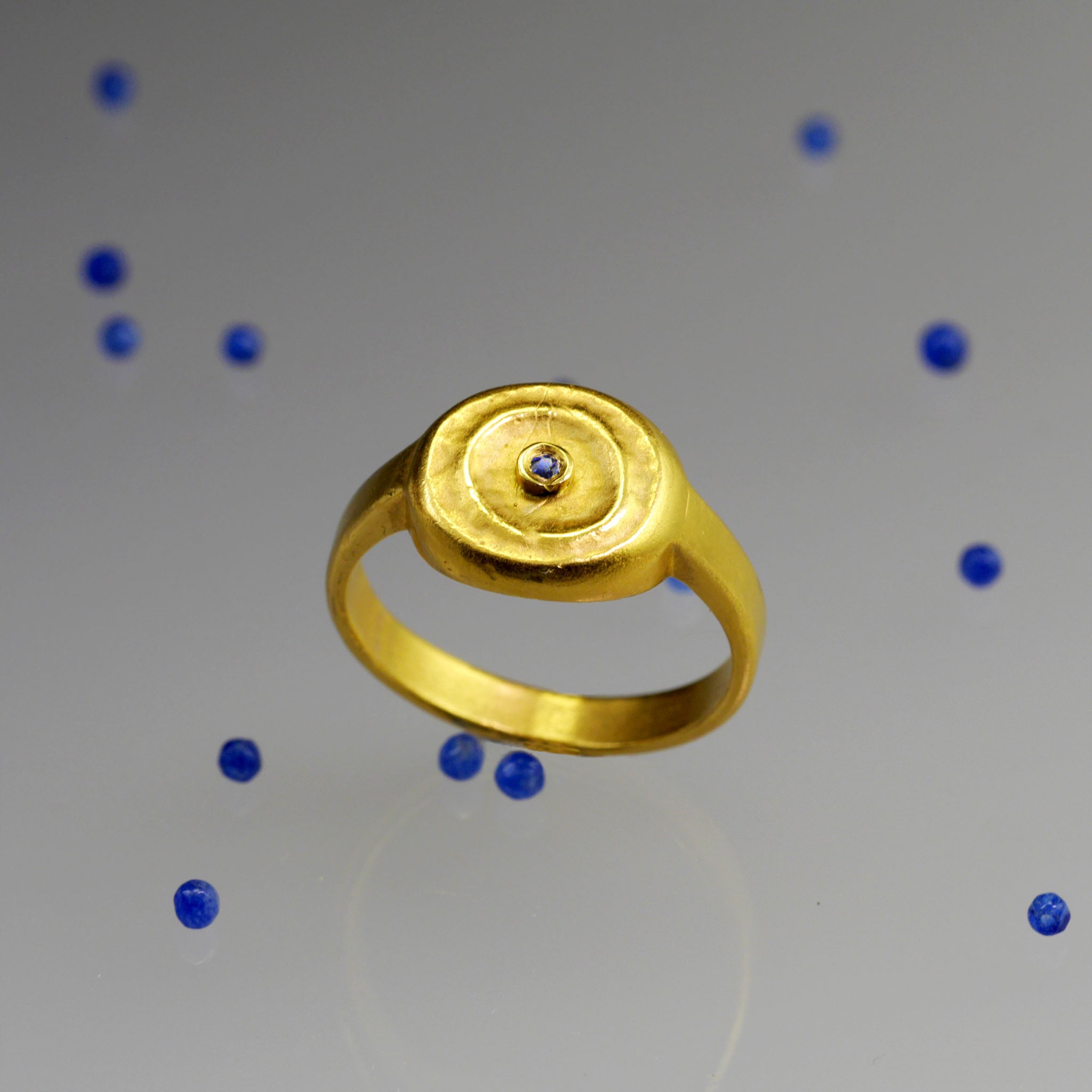 Top view of Handmade 18k Gold ring with a central Sapphire and tiny Sapphire beads scattered around it, exuding vintage charm reminiscent of the Egyptian pharaohs' era.