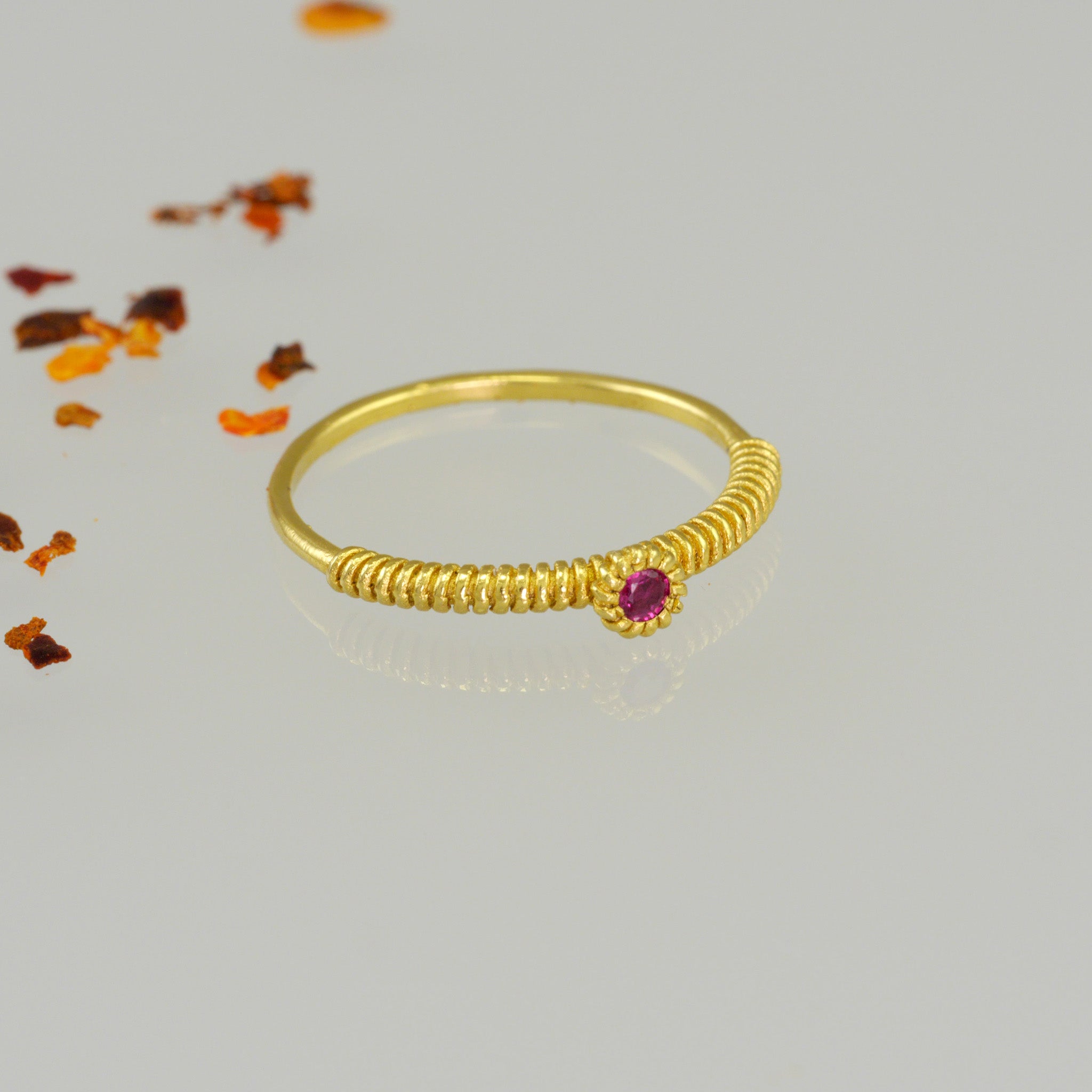 A thin gold ring with a coiled gold string, showcasing a vivid Ruby at its center. Elegant and charming, it radiates subtle allure.