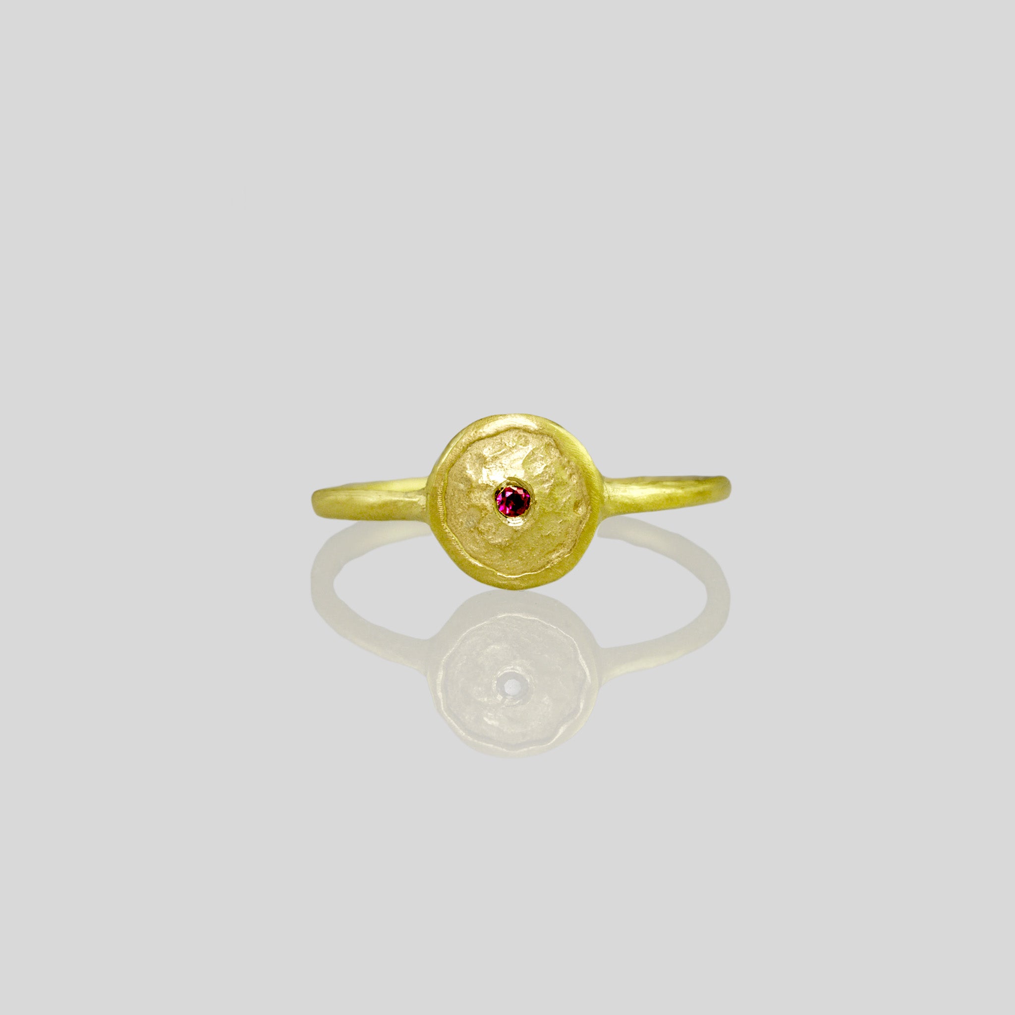 Front view of an Hand-crafted 18k Gold Ring with a small Ruby set in the center of a circular plate, resembling a shining star in the sky. Delicate and elegant, radiating brilliance.