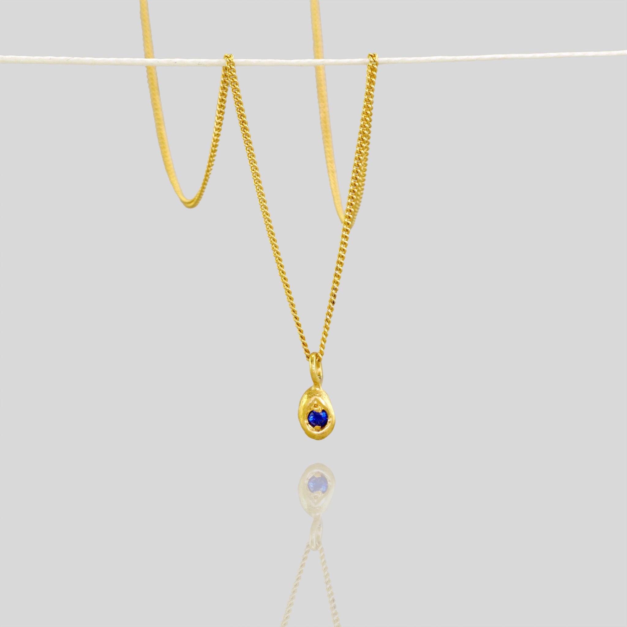 18k Yellow Gold Pendant with a drop shape and a central sapphire, designed to replicate a naturally gathered dried seed.