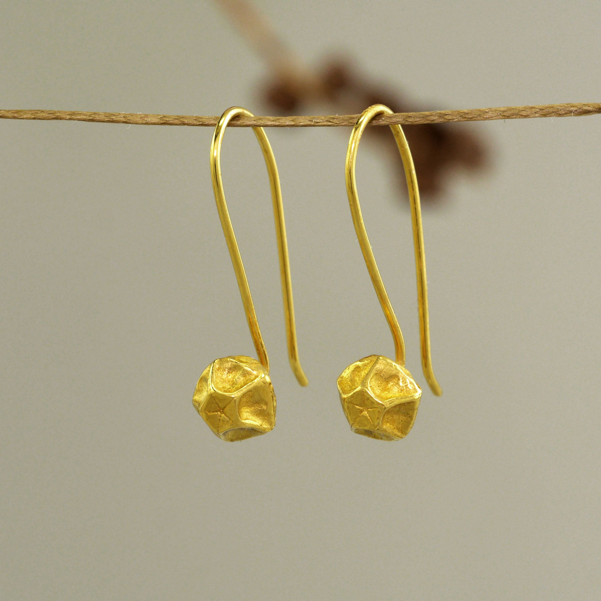 Handcrafted Gold Pentagon Earrings with Intricate Lines hanging from a natural thresd.