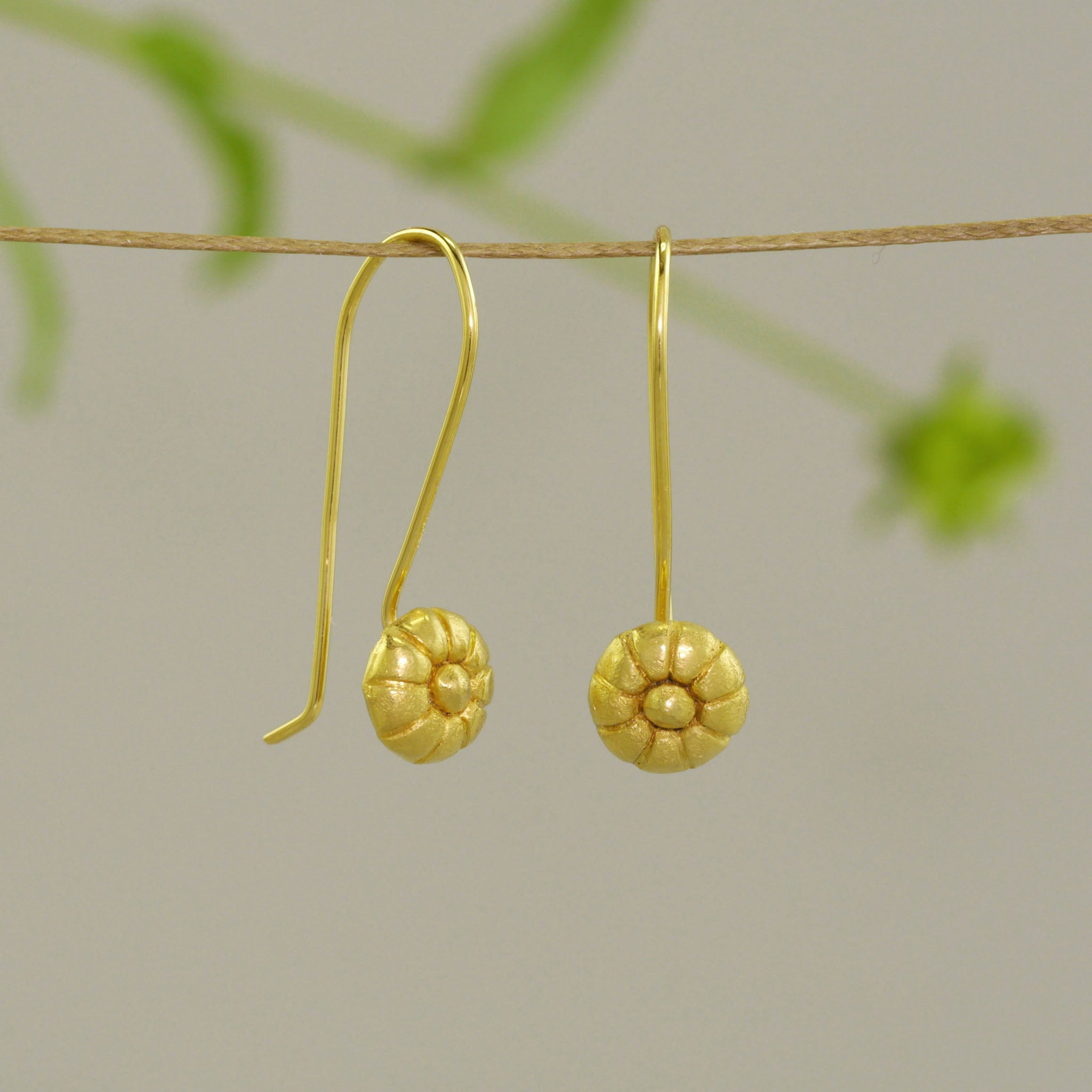 Mallow Fruit-inspired Gold Drop Earrings hanging from a natural thread with natural background.