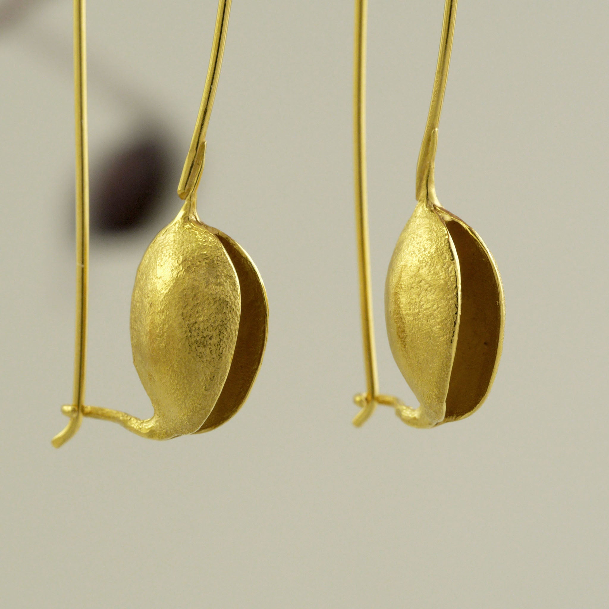 close up of Nature-inspired Gold drop earrings, replicating captivating dried seeds. Minimalistic, chic, and elegant, embodying natural beauty and femininity.