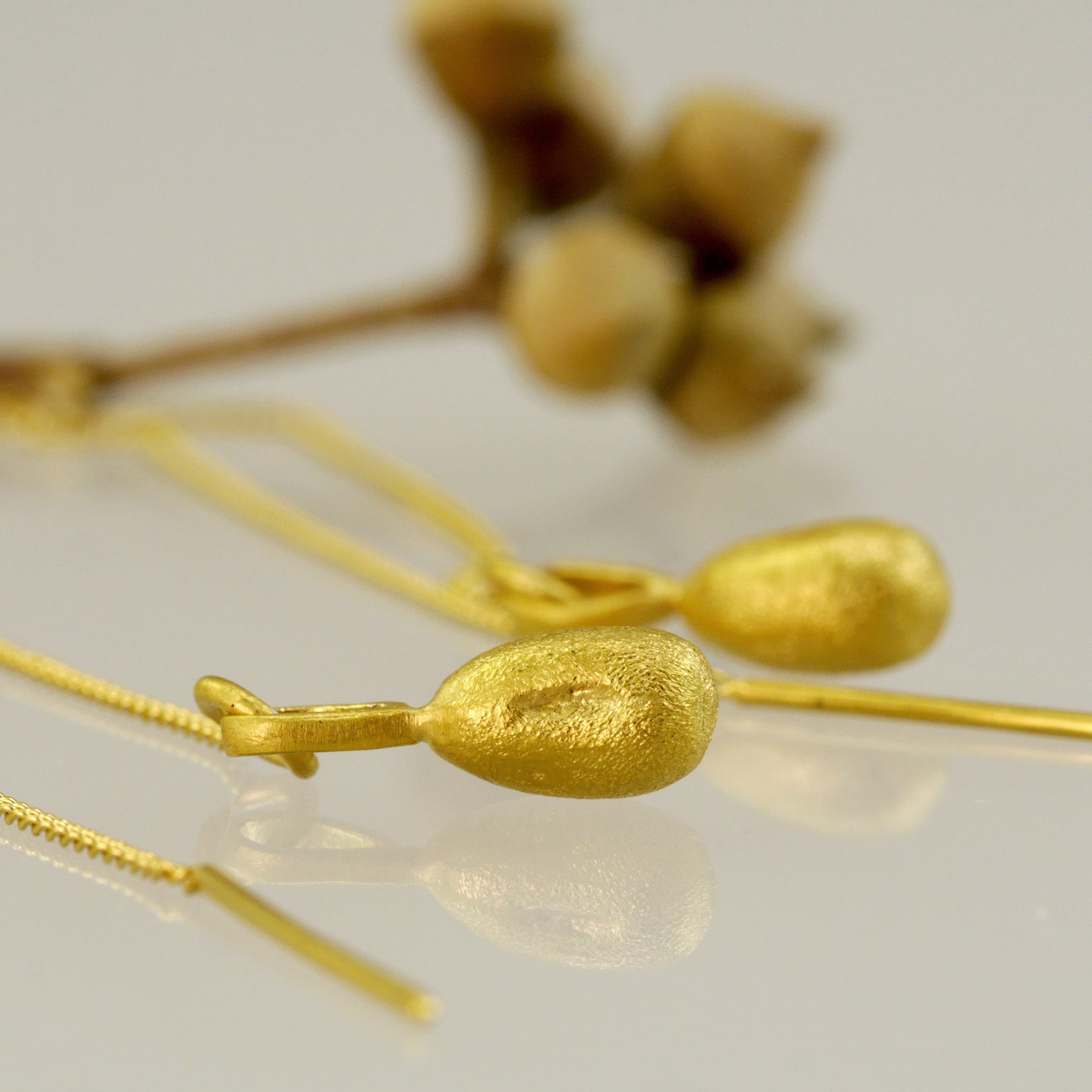 close up of Nature-inspired gold earrings with delicate chains and needle-tip attachments,with natural seeds in the background.