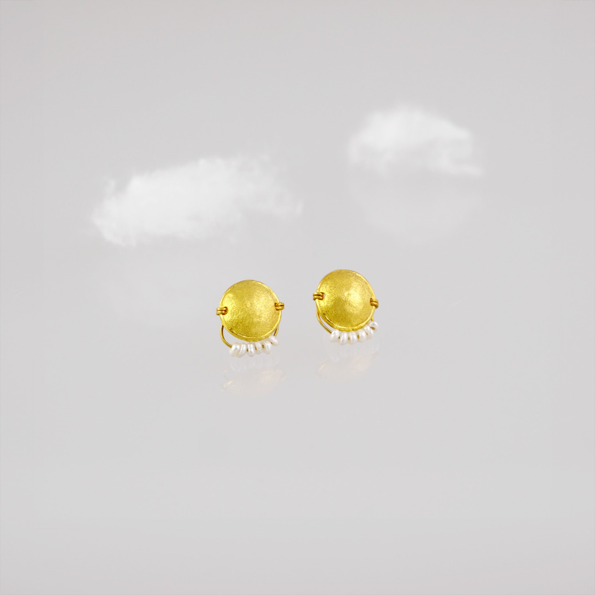 Hand-crafted 18k gold stud earrings with a curved disk design, adorned with a delicate golden thread and tiny pearls hanging from a golden bow.