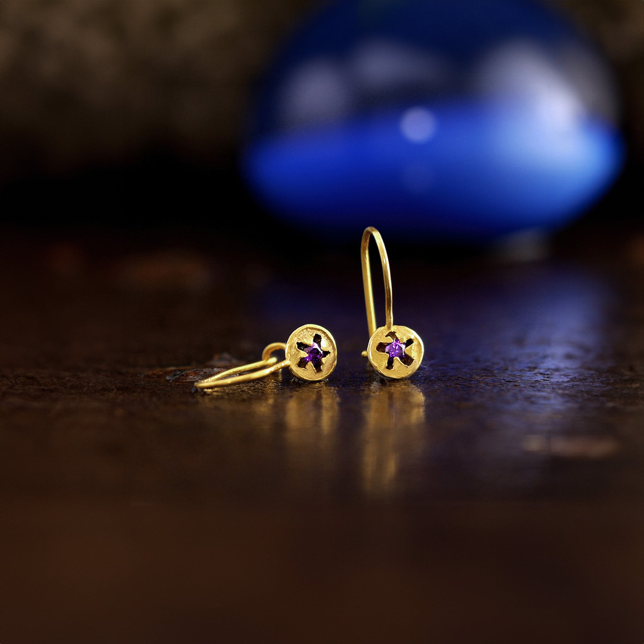 Delicate drop earrings in yellow gold, inspired by eucalyptus seeds, featuring a central inlaid amethyst stone with a dark rusty background.