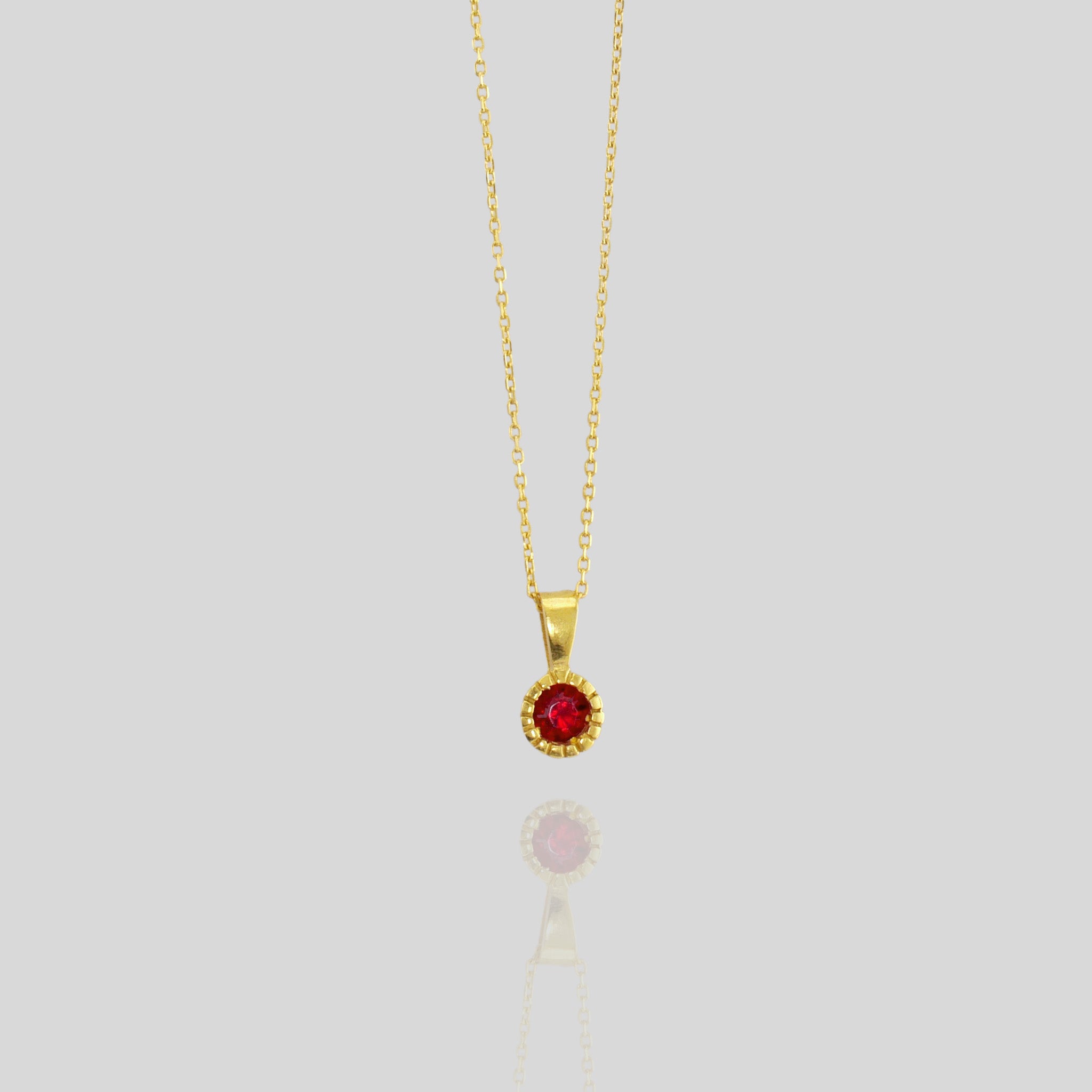 Close up of an Elegant round gold pendant with embroidered texture and central Ruby, exuding classic sophistication.