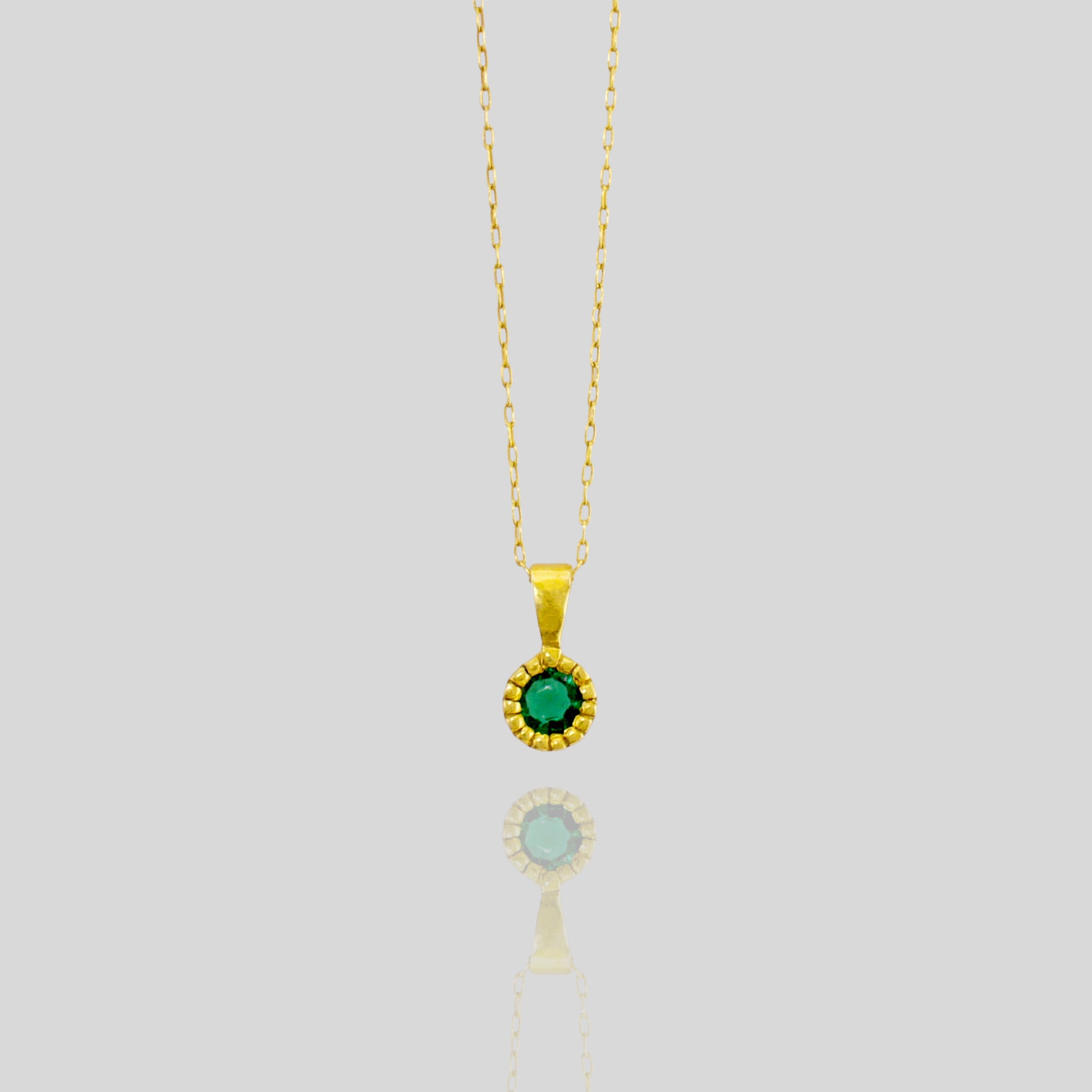 Close up of an Elegant round gold pendant with embroidered texture and central Emerald, exuding classic sophistication.