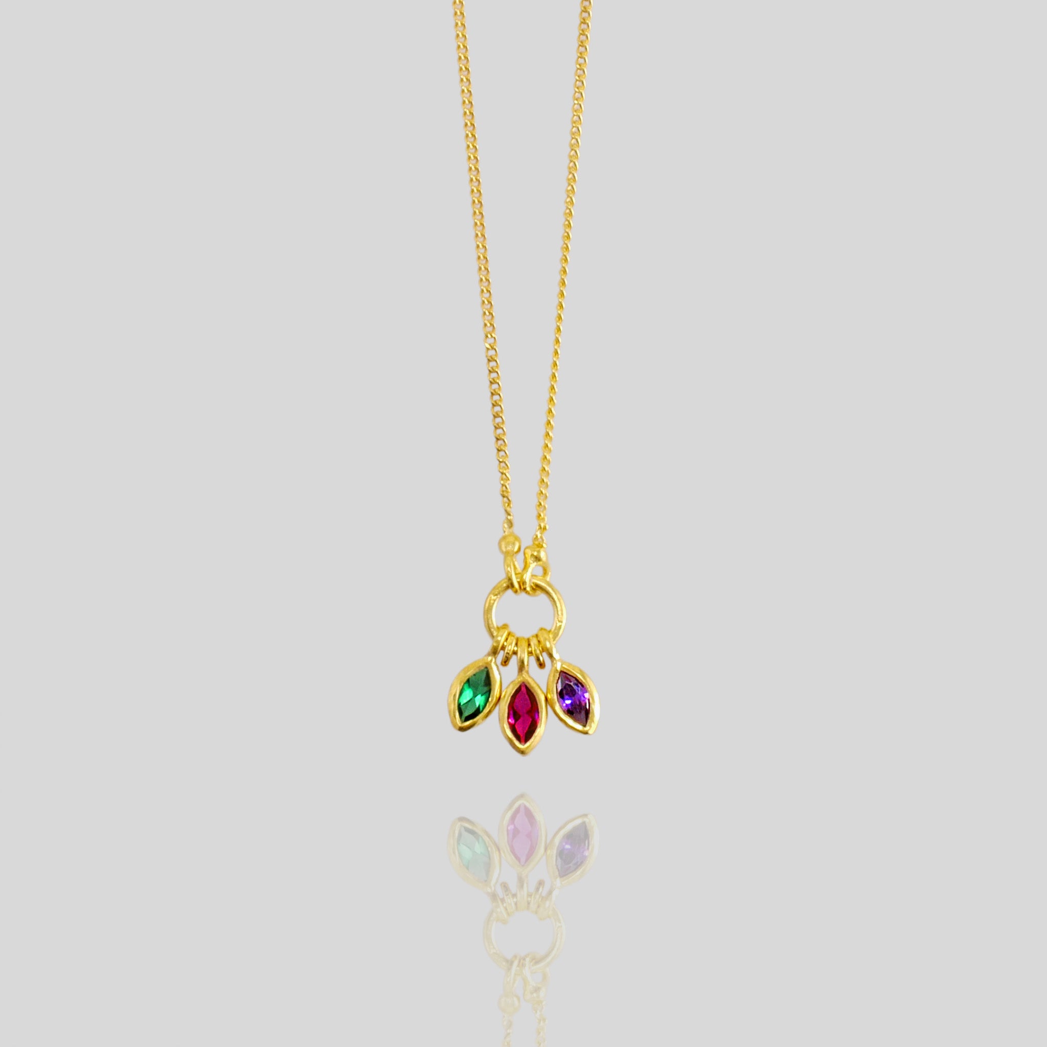 Close up of a Gold marquee pendant with three expertly cut gemstones - ruby, emerald, and sapphire - elegantly intertwined, showcasing a blend of colors and radiance.