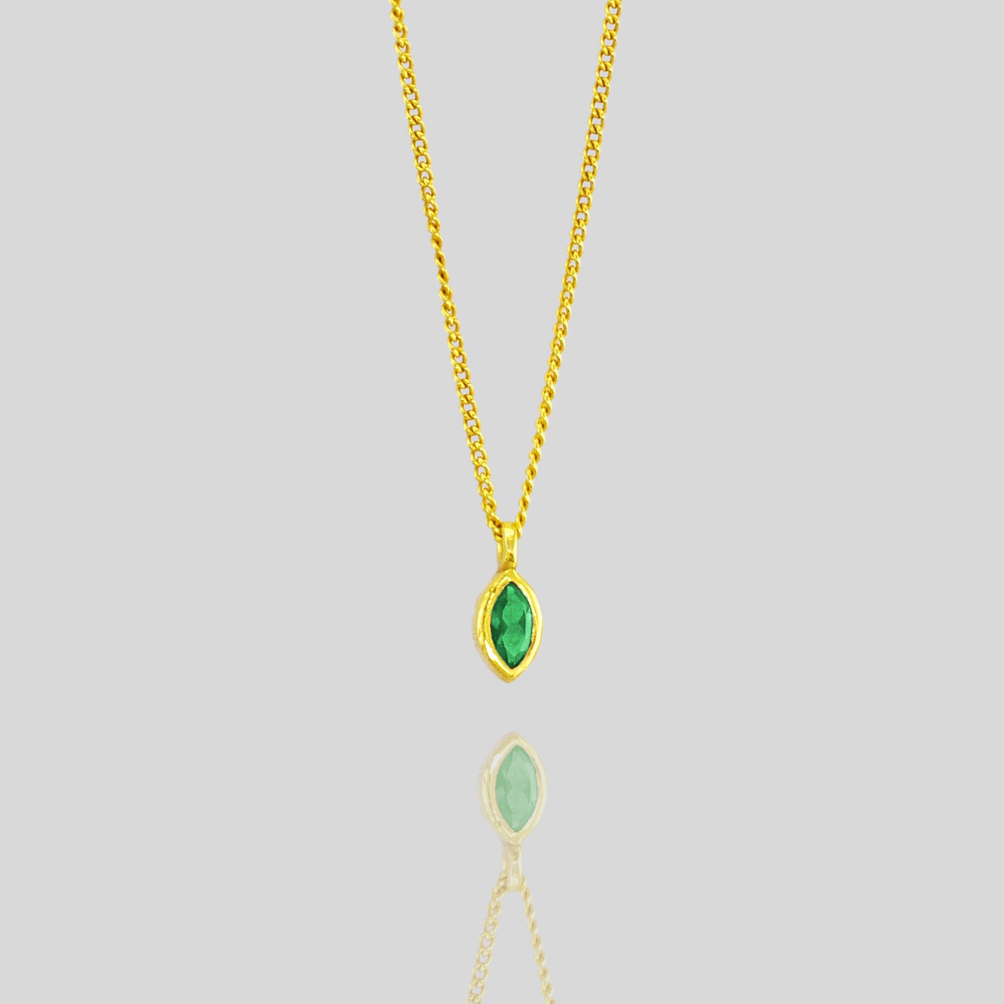 Detail of the Elegant marquee gold pendant featuring a small, exquisite emerald, adding a delicate touch of vibrant green to enhance any outfit with sophistication.