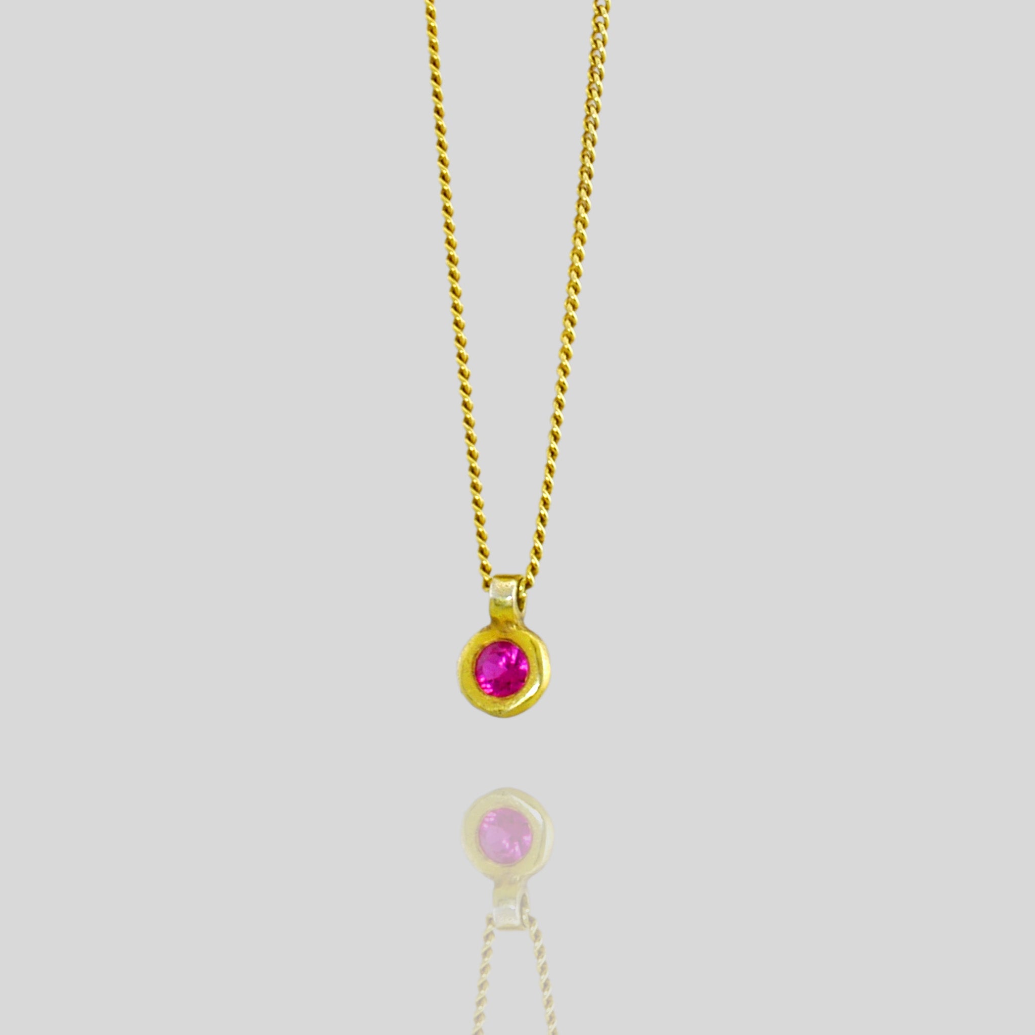 Close up of a Classic round 18k Gold pendant with vibrant red ruby, symbolizing July birthstone and associated with love, passion, and prosperity.