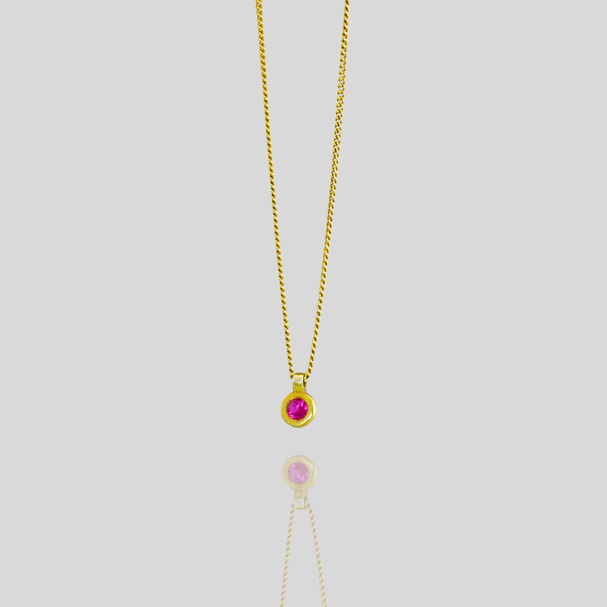 Classic round 18k Gold pendant with vibrant red ruby, symbolizing July birthstone and associated with love, passion, and prosperity.