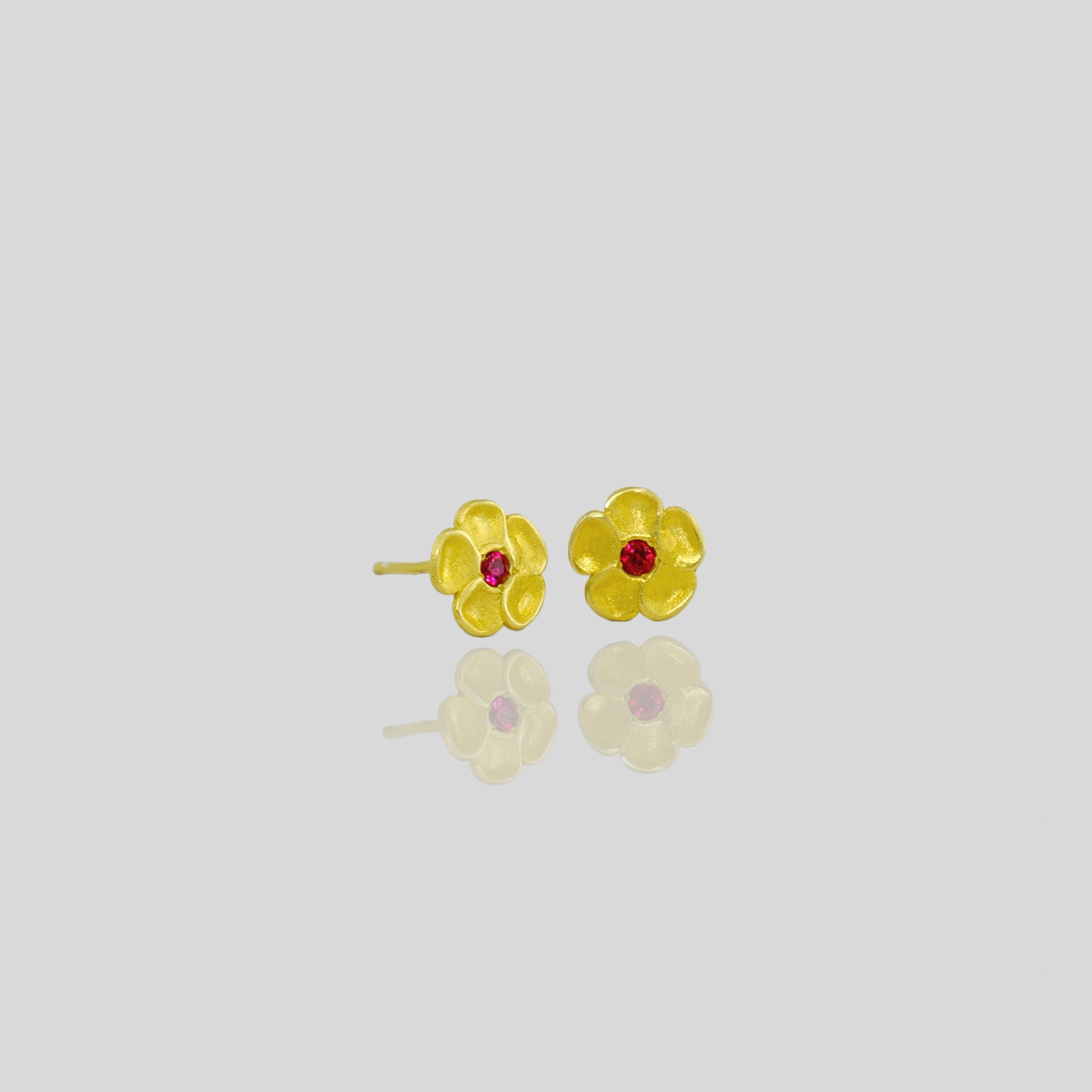Delicate yellow gold flower stud earrings with a sparkling ruby center. Perfect for any occasion!
