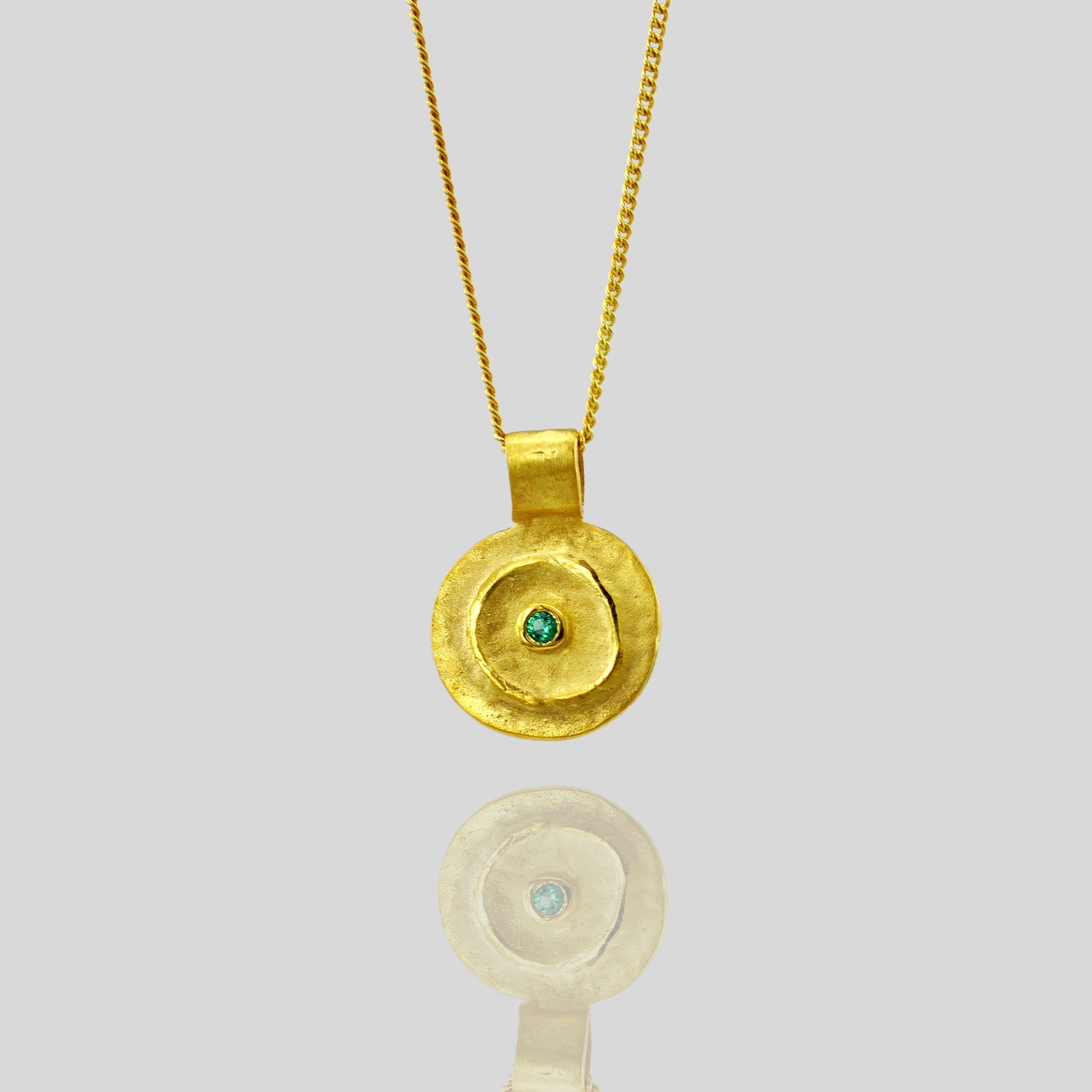 Close up of Pharaohs I - Ancient round gold pendant with a vivid Emerald gemstone at its center, reminiscent of the opulent jewelry of the Egyptian Pharaohs' era, crafted from yellow gold.