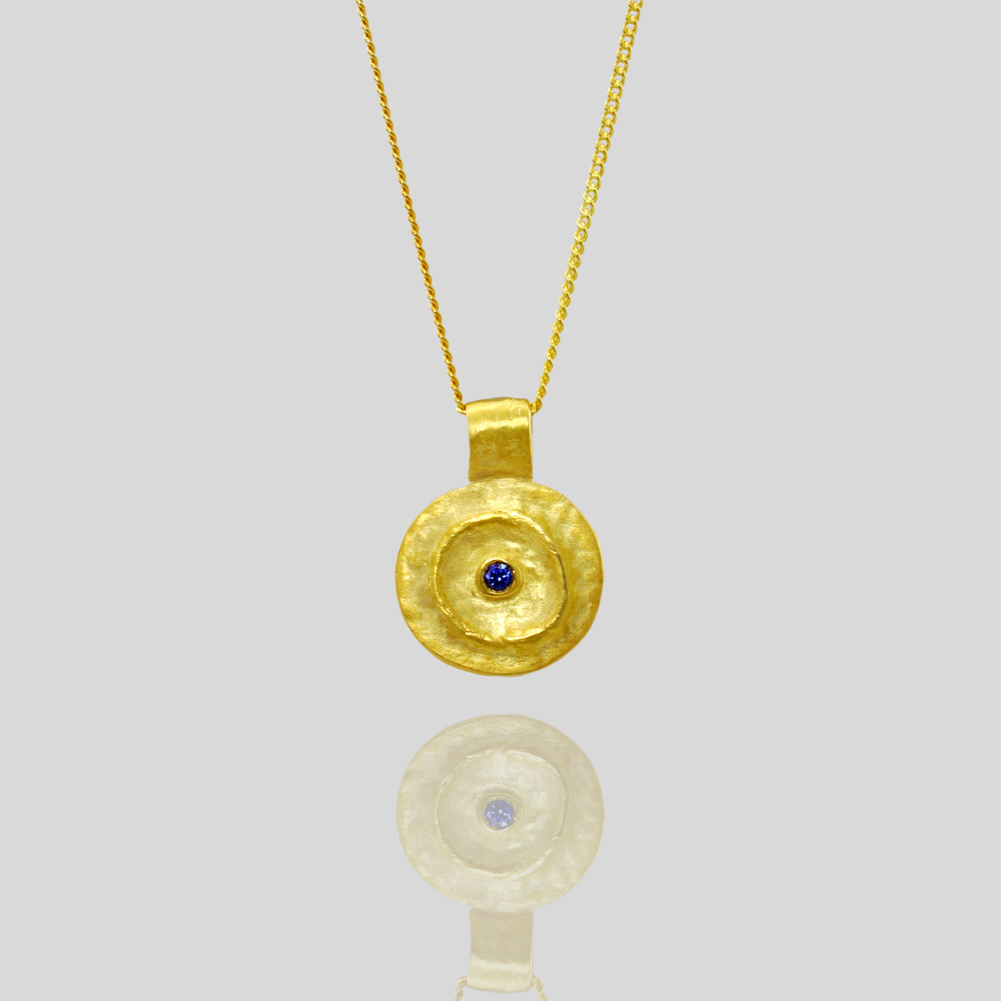 Detail of Pharaohs I - Ancient round gold pendant with a vivid Sapphire gemstone at its center, reminiscent of the opulent jewelry of the Egyptian Pharaohs' era, crafted from yellow gold.