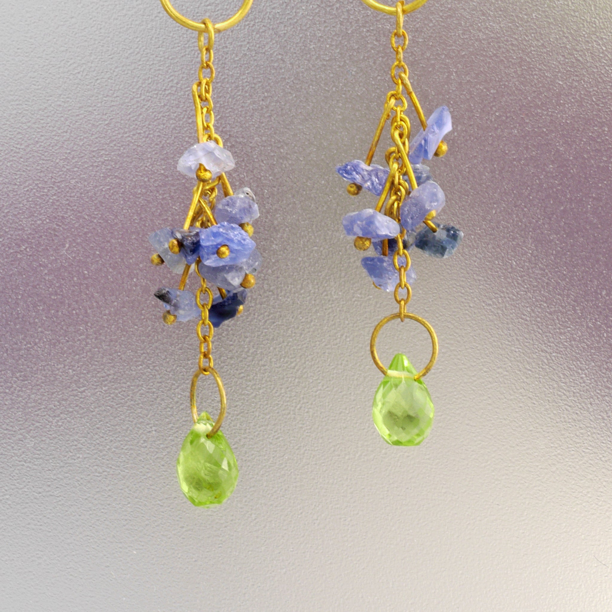 Details of 18k Yellow Gold earrings adorned with raw blue sapphires and a dangling Peridot drop.