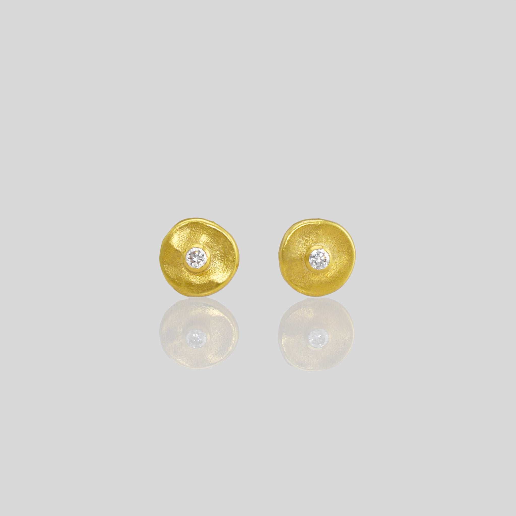 Close up of hand-crafted gold stud earrings with a round amorphous shape, featuring a diamond set in the center.